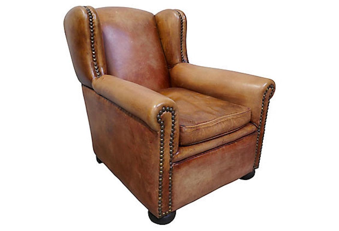 Vintage French leather wingback club chair. Original natural tanned sheepskin with bronze patina hand-hammered nailhead detailing. Feather/down loose seat cushion with zipper closure.