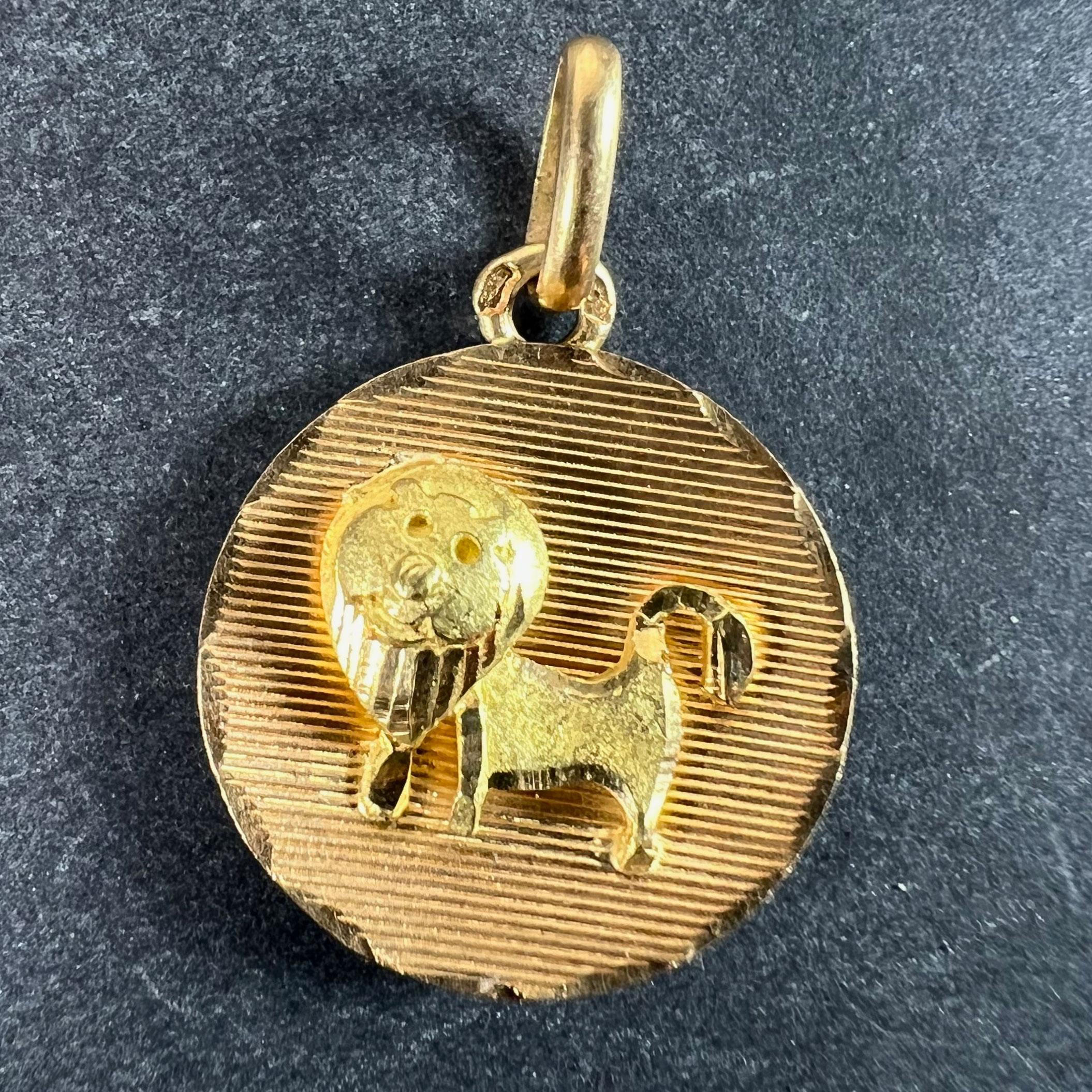 Un ciondolo charme francese in oro giallo 18 carati (18K) disegnato come una medaglia rotonda concava incisa con linee orizzontali con un leone opaco in rilievo attaccato al centro, che rappresenta il segno zodiacale del Leone all'interno di una