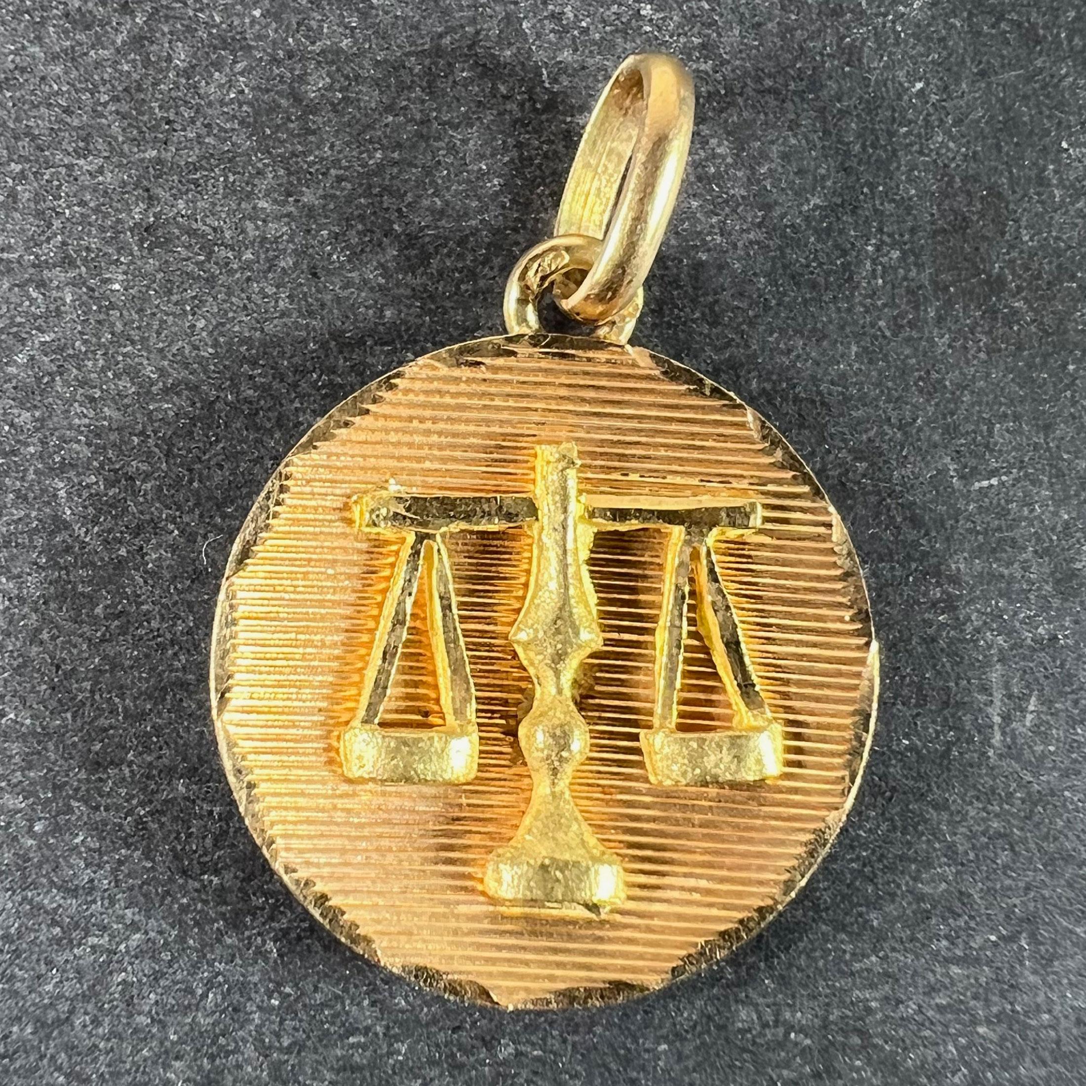 Pendentif à breloques en or jaune 18 carats (18K) conçu comme une médaille ronde concave gravée de lignes horizontales avec une paire d'écailles en relief mat attachée au centre, représentant le signe astrologique de la Balance dans un cadre