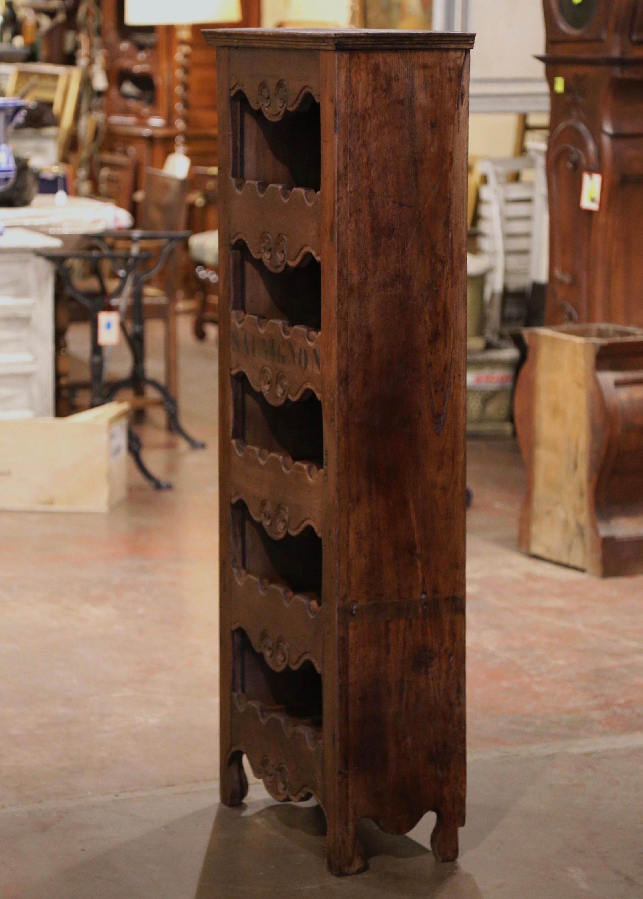 This narrow, antique wine storage cabinet was crafted in western France using old timber. Built of pine wood, the tall and thin cabinet sits on four small scroll feet under a scalloped apron. The piece features five shelves embellished with