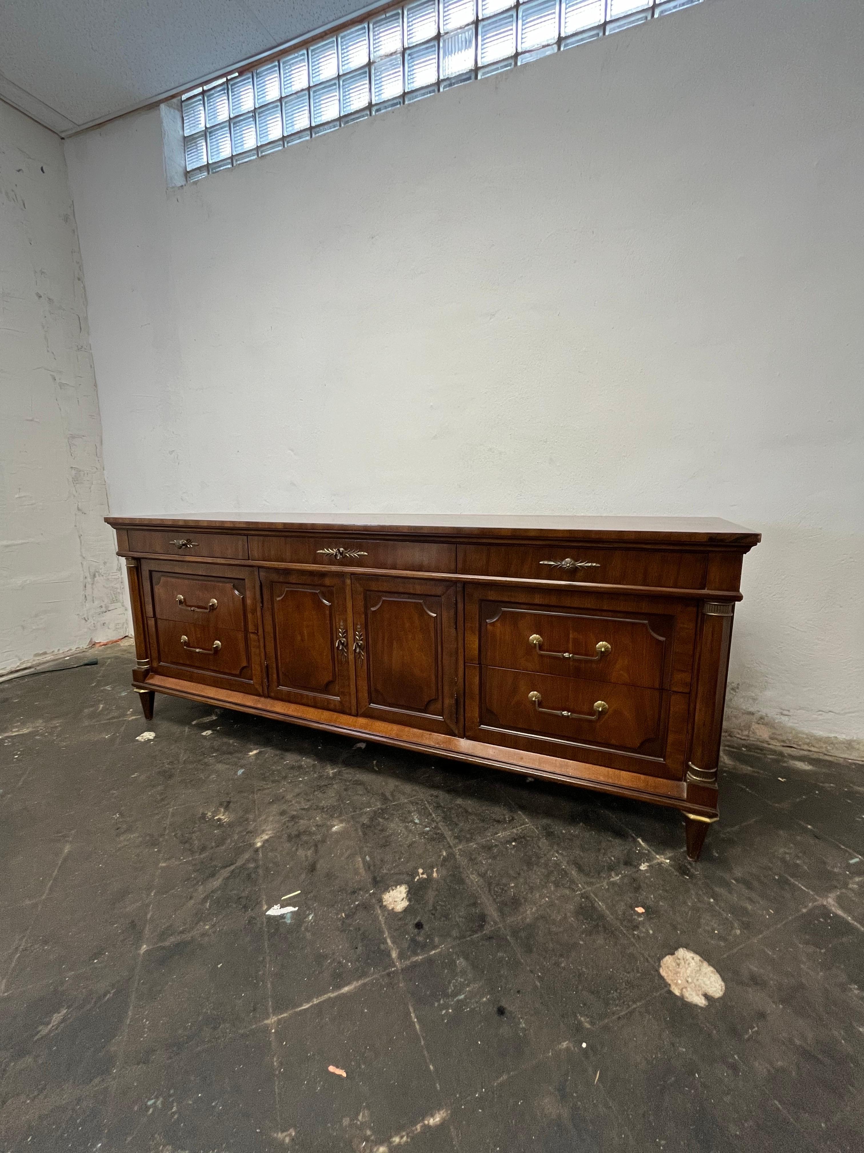 Stunning long dresser in the Louis XV or Empire style. Solid and heavy. 9 drawers with brass hardware. Beautiful wood grain and columnar fronts capped with brass banding.