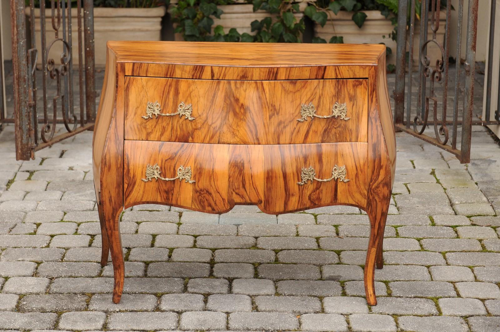 A vintage French Louis XV style olivewood veneered two-drawer bombé chest from the mid-20th century, with scalloped skirt and cabriole legs. Born in France during the midcentury period, this exquisite commode features a serpentine front top, sitting