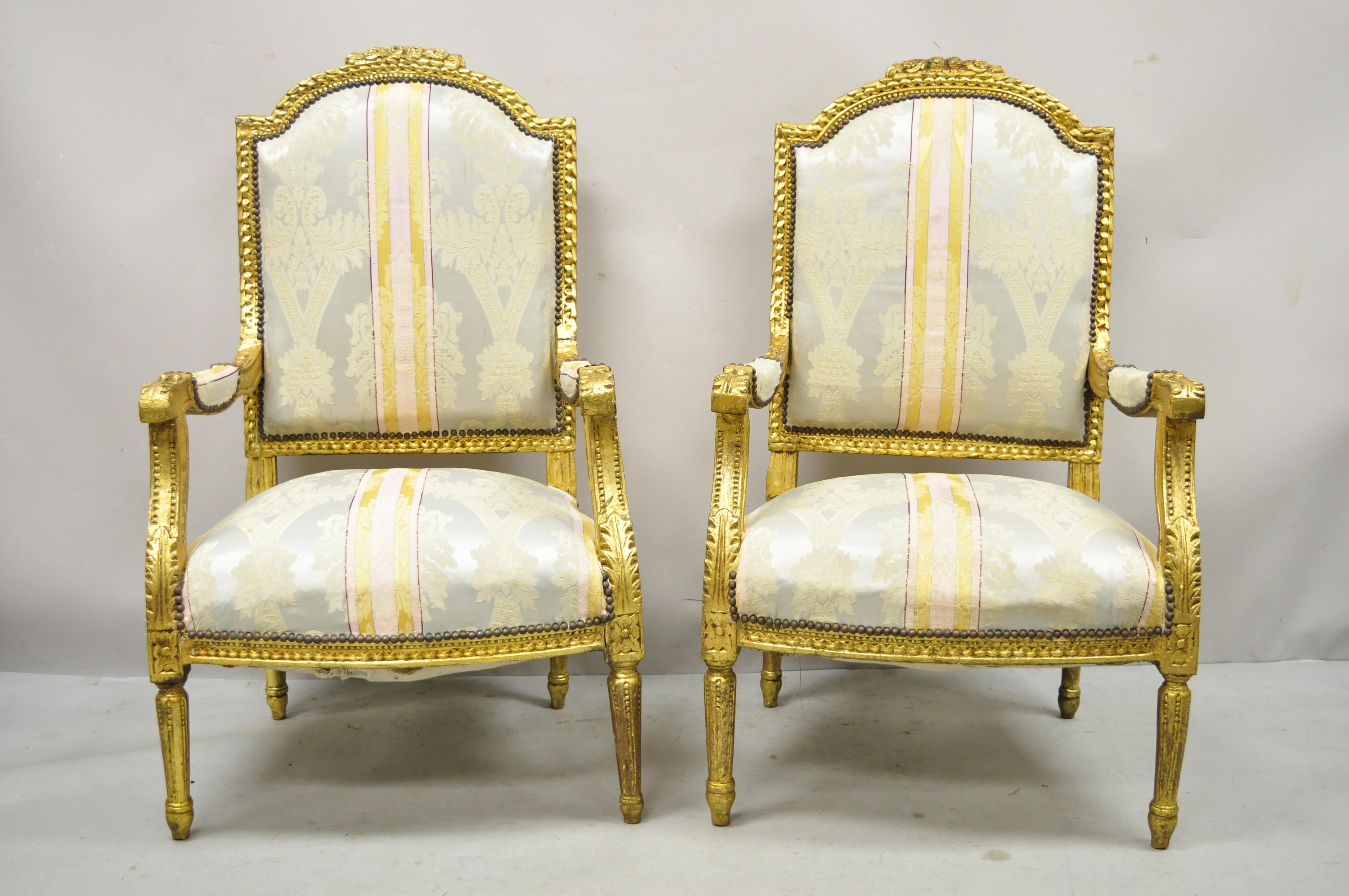 Vintage French Louis XVI carved gold giltwood upholstered lounge arm chairs (A) - a Pair. Item features distressed gold gilt finish, floral carved details, solid wood frames, tapered legs, great style and form. Circa Late 20th Century. Measurements: