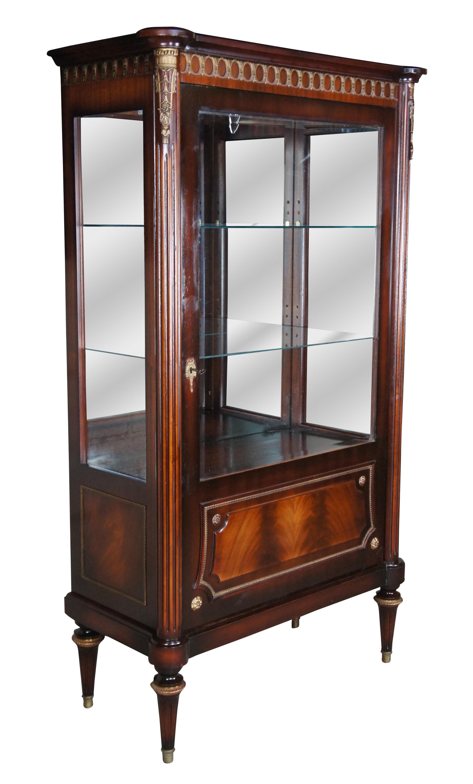 Vintage French Louis XVI inspired display cabinet. Made in Cairo Egypt (Arabska Republika Egiptu) by Abbas, circa 1972. Made mahogany with crotch mahogany front. Features ornate brass ormolu, reeded columns and turned tapered legs with brass caps.