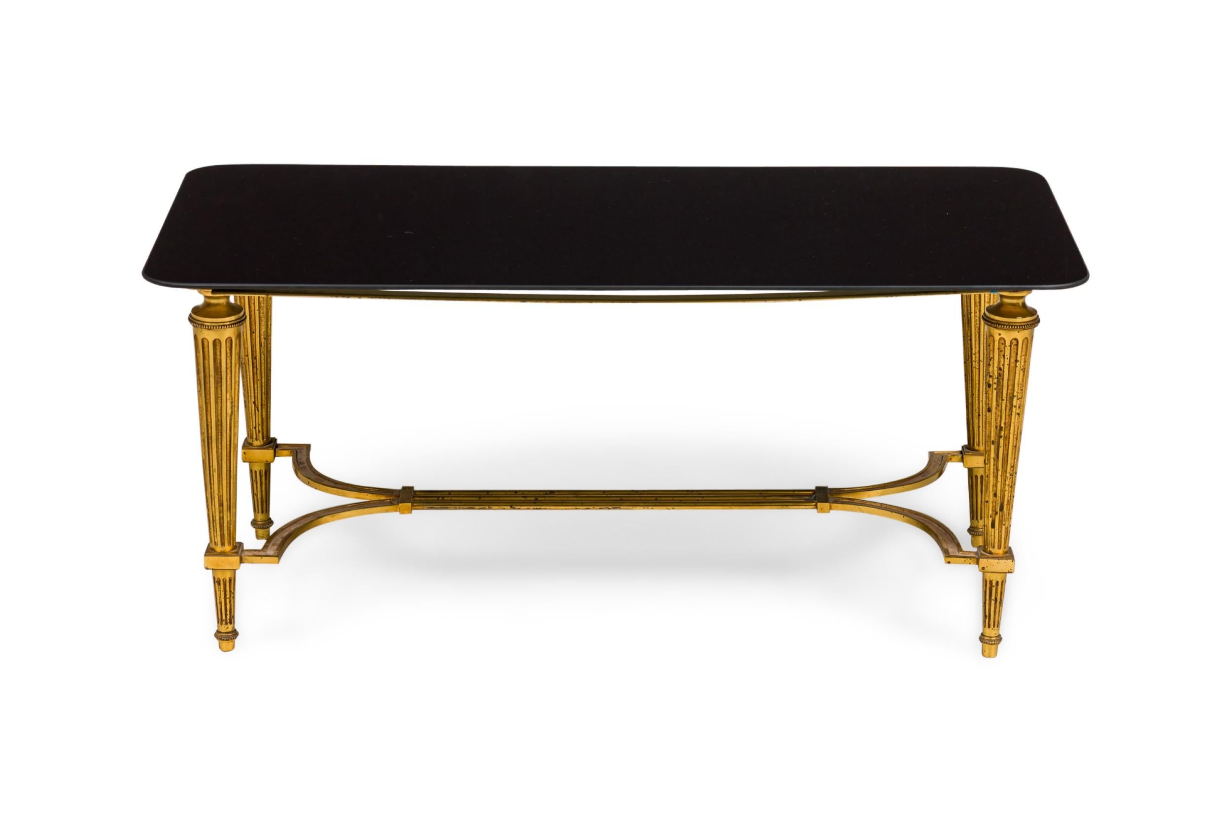 Mesa de centro rectangular de latón estilo Luis XVI de época francesa, con patas acanaladas de latón unidas por una camilla y tablero de cristal negro.