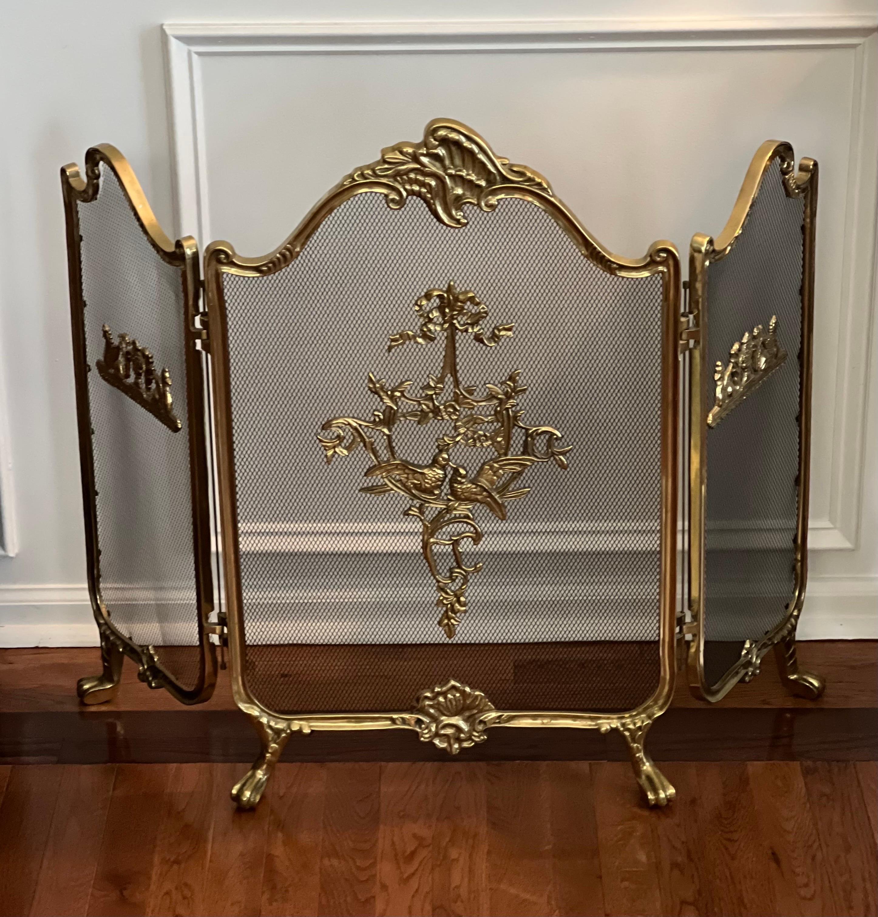 Fabulous vintage French Louis XVI style brass fireplace screen.

The screen features three folding panels upon claw feet. Adorned with brass ornaments of love birds amongst foliage with side panel motifs of gryphons and amphorae. The larger middle