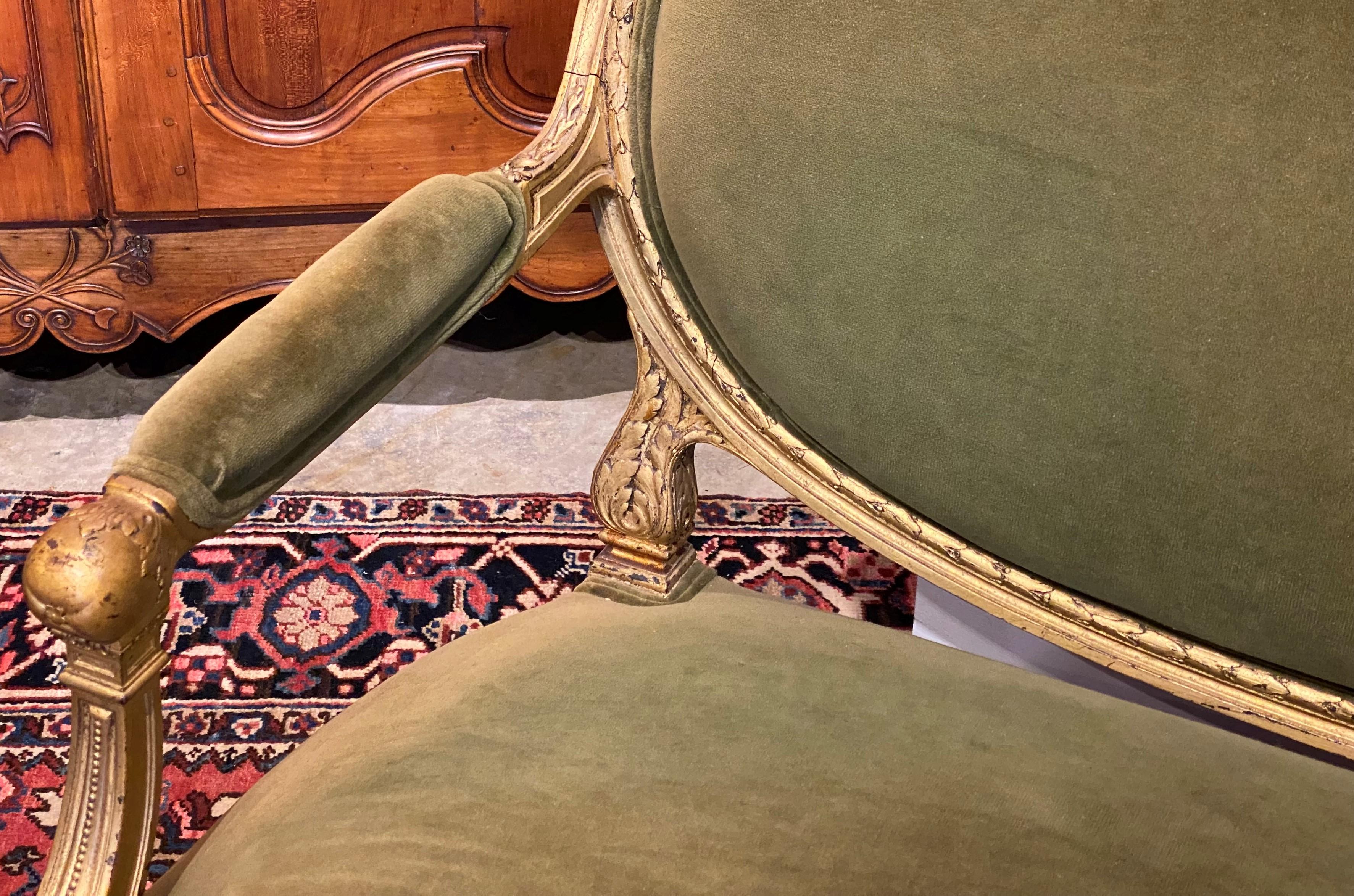 A fine antique French Louis XVI style giltwood sofa or settee with oval upholstered back with small carved shell or fan center crest, padded arms, and a foliate decorated giltwood frame with olive green velvet upholstery, all supported by four 