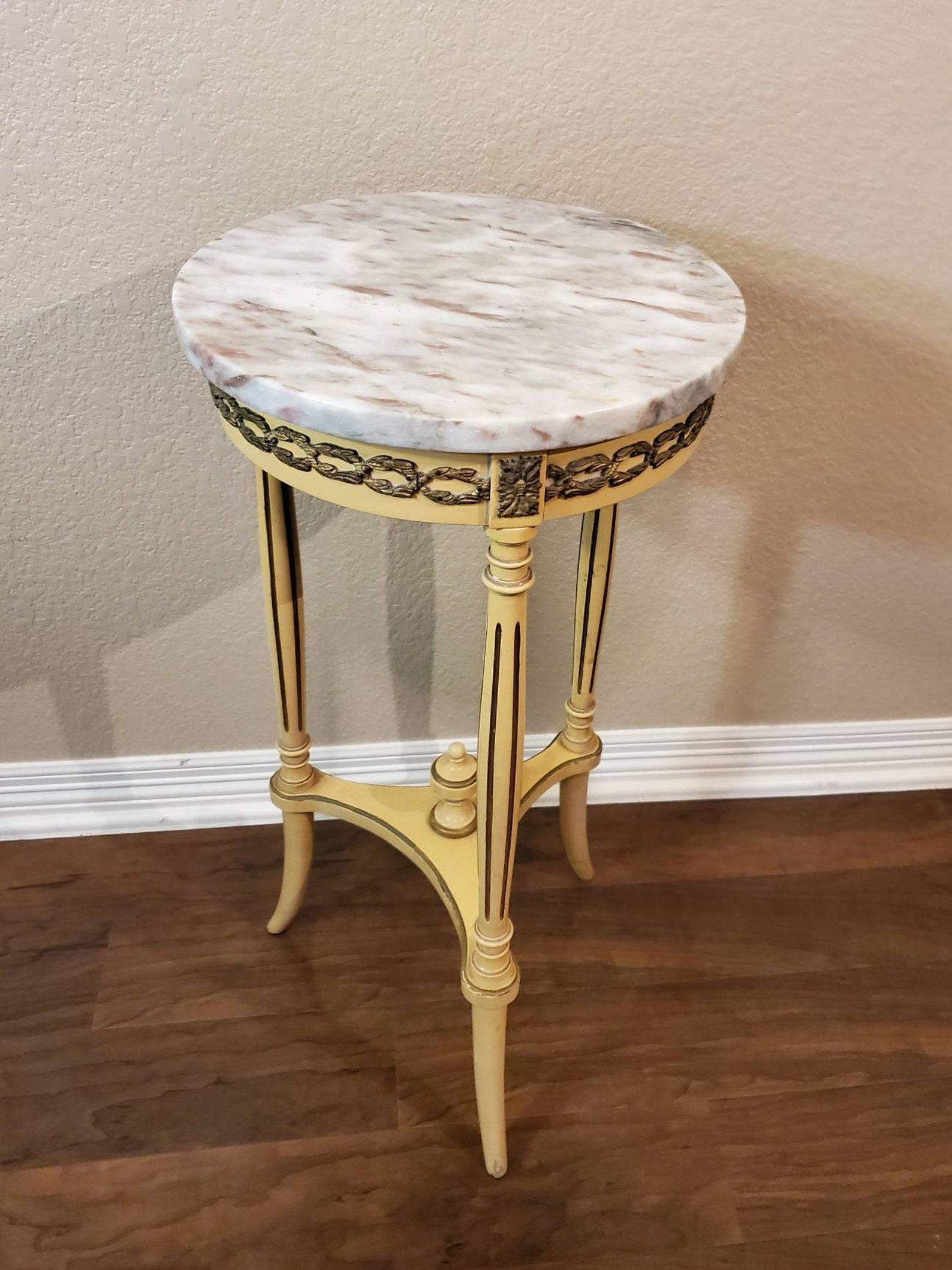 A chic Louis XVI style pedestal table or stand. Hand crafted in France during the first half of the 20th century, it features a circular marble top, above the swag wreath gilt-ormolu mounted hand carved and painted hardwood frame, joined by