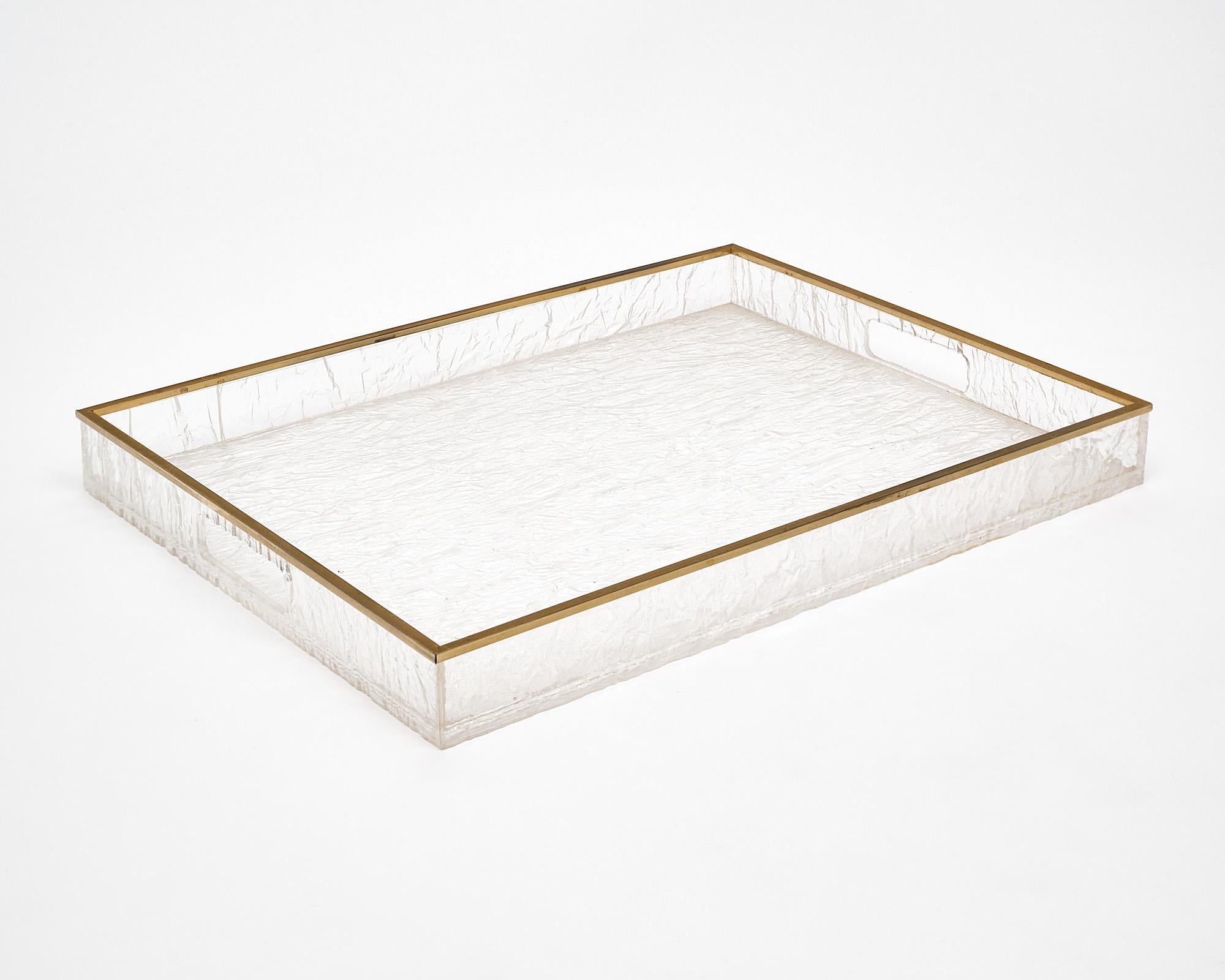 Tray table from France featuring a Lucite x-shape base that folds out to support a Lucite tray top. The Lucite tray is framed with brass trim and features a textured pattern throughout the Lucite.

