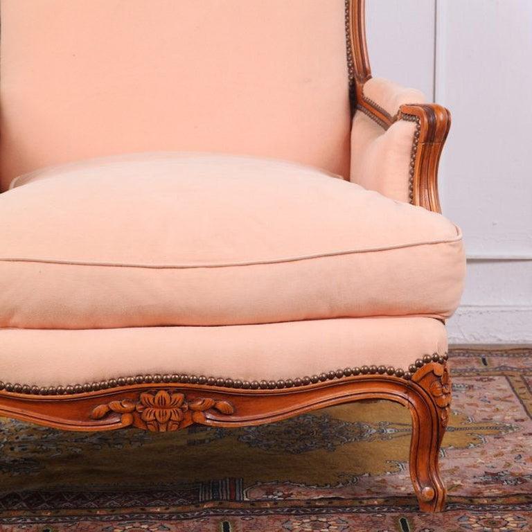 A mid-20th century French vintage Louis XV style cherry wood-framed armchair or bergère with carved floral details to the frame and scrolled carved feet.