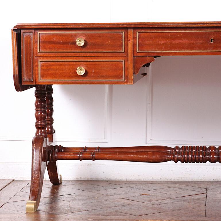 Vintage French Directoire style desk in mahogany, having a gilt-tooled leather top and further drop-leaf surfaces to each end. Drawers with brass trim fitted to the frieze and corresponding false drawers to the reverse, and raised on turned supports