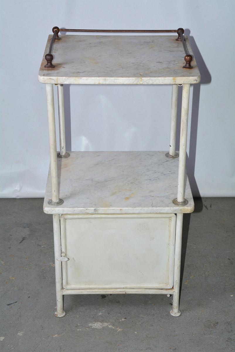 The vintage metal night stand or medical cabinet has two veined marble shelves, the top one having a metal railing on three sides. Below the bottom shelf is a metal storage cabinet. Perfect additional storage and shelving for the bathroom, kitchen,