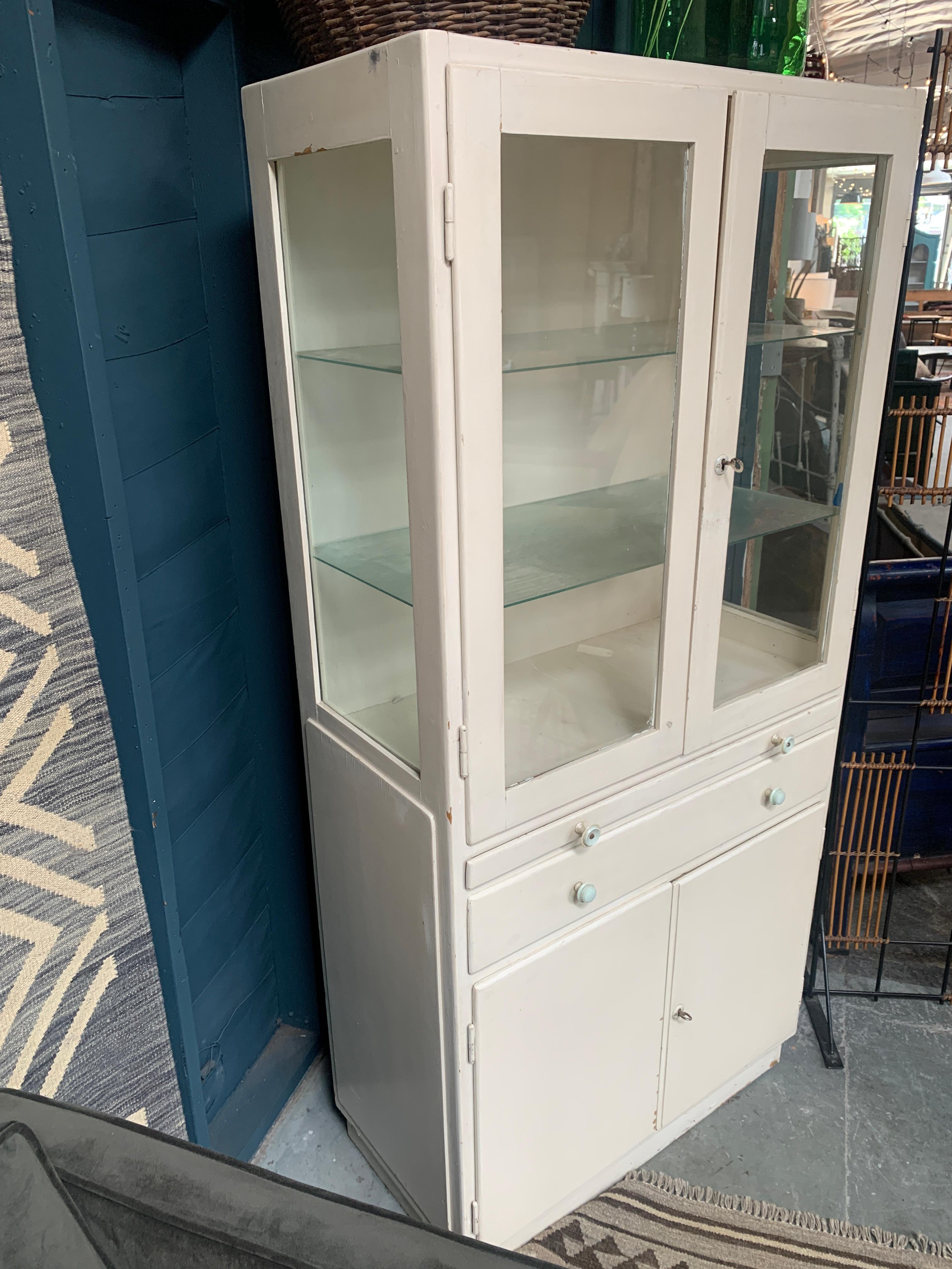Vintage French Medicine cabinet has ample amount of storage whether it be used as a display case or book shelf. Features two glass shelves, pullout board, drawer, and shelf but;t into bottom storage.