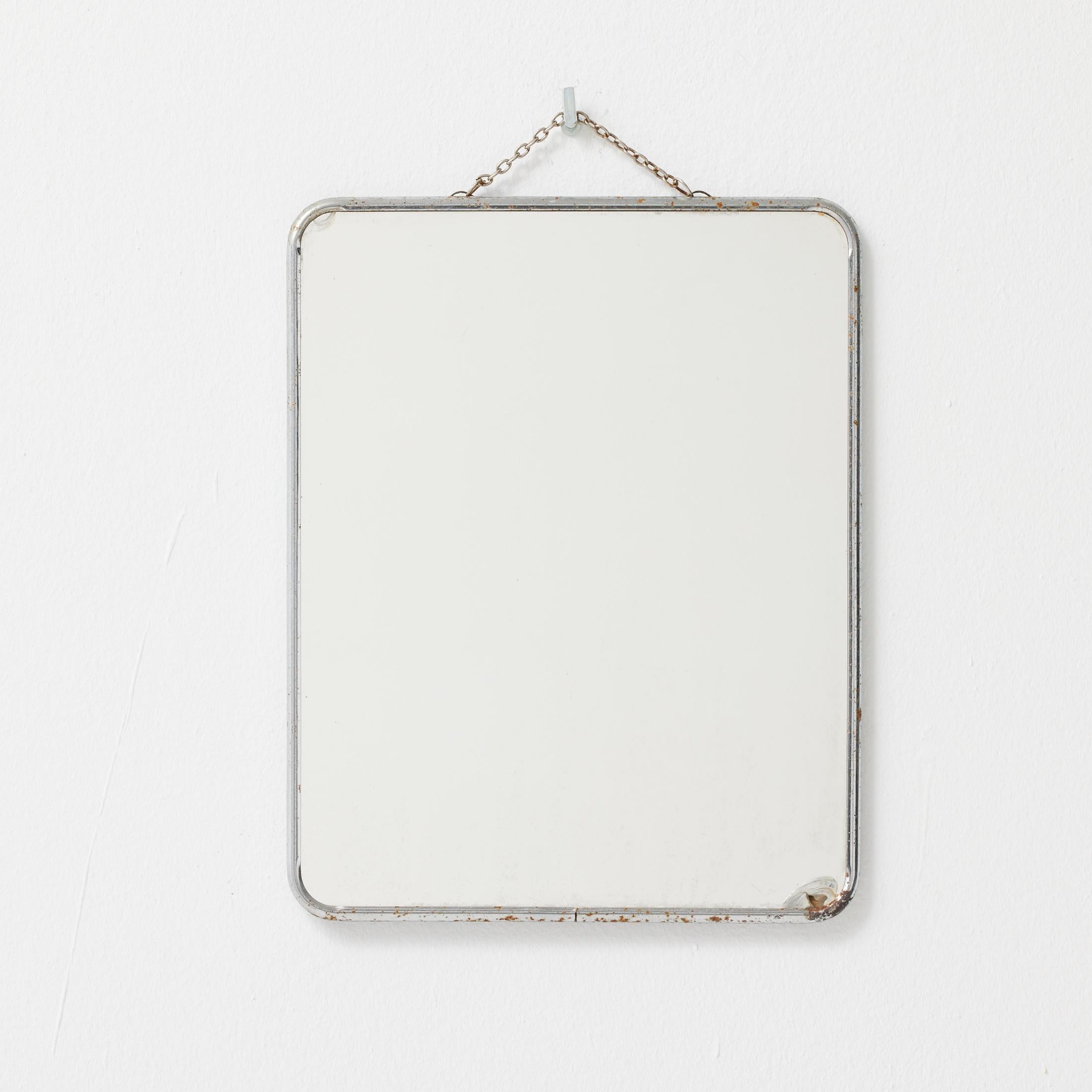 Un charmant et authentique miroir mural français des années 1940, qui a conservé sa vitre, son cadre métallique et sa chaîne de suspension d'origine. Le miroir présente une forme rectangulaire minimaliste avec des coins légèrement arrondis et une