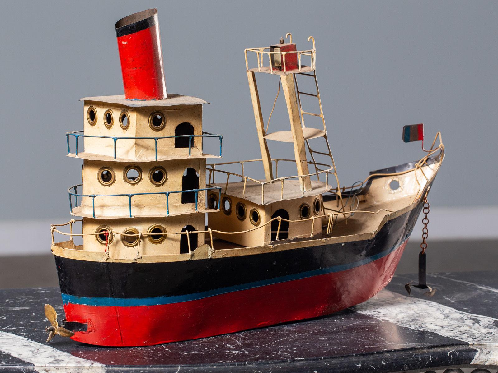 A vintage French toy metal freighter, circa 1950. This float worthy toy boat originally had a small battery operated moter inside the hull to drive the propeller and light the top Signal beacon. Definitely showing the passage of time the painted