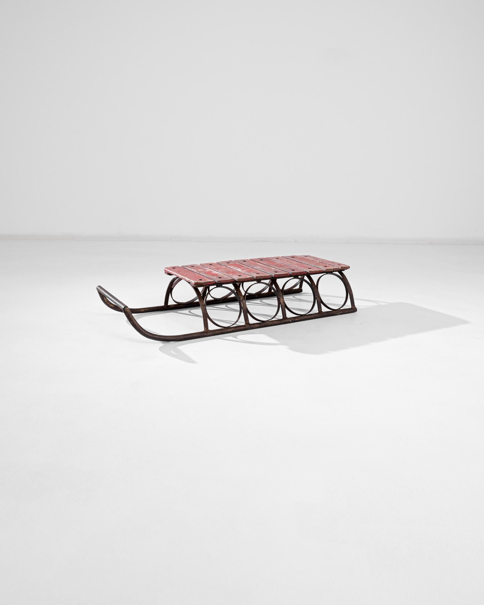 A 20th century metal sledge with a wooden seat, produced in France. A wrought iron circle structure supports candy red boards with a beautiful original patina. An antique with a heart, this versatile sledge can serve as a bench as well as a