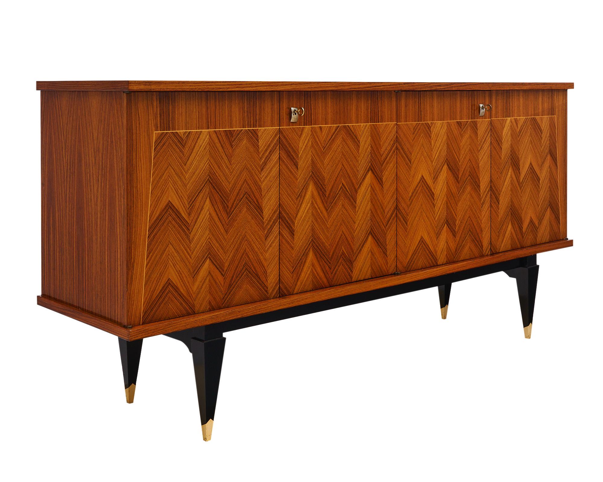 Buffet from mid-century France made with a Rosewood veneer in a striking chevron pattern. There is an ebonized base with four tapered legs capped in brass. There are four doors that open to reveal a lemon wood interior with shelves and two