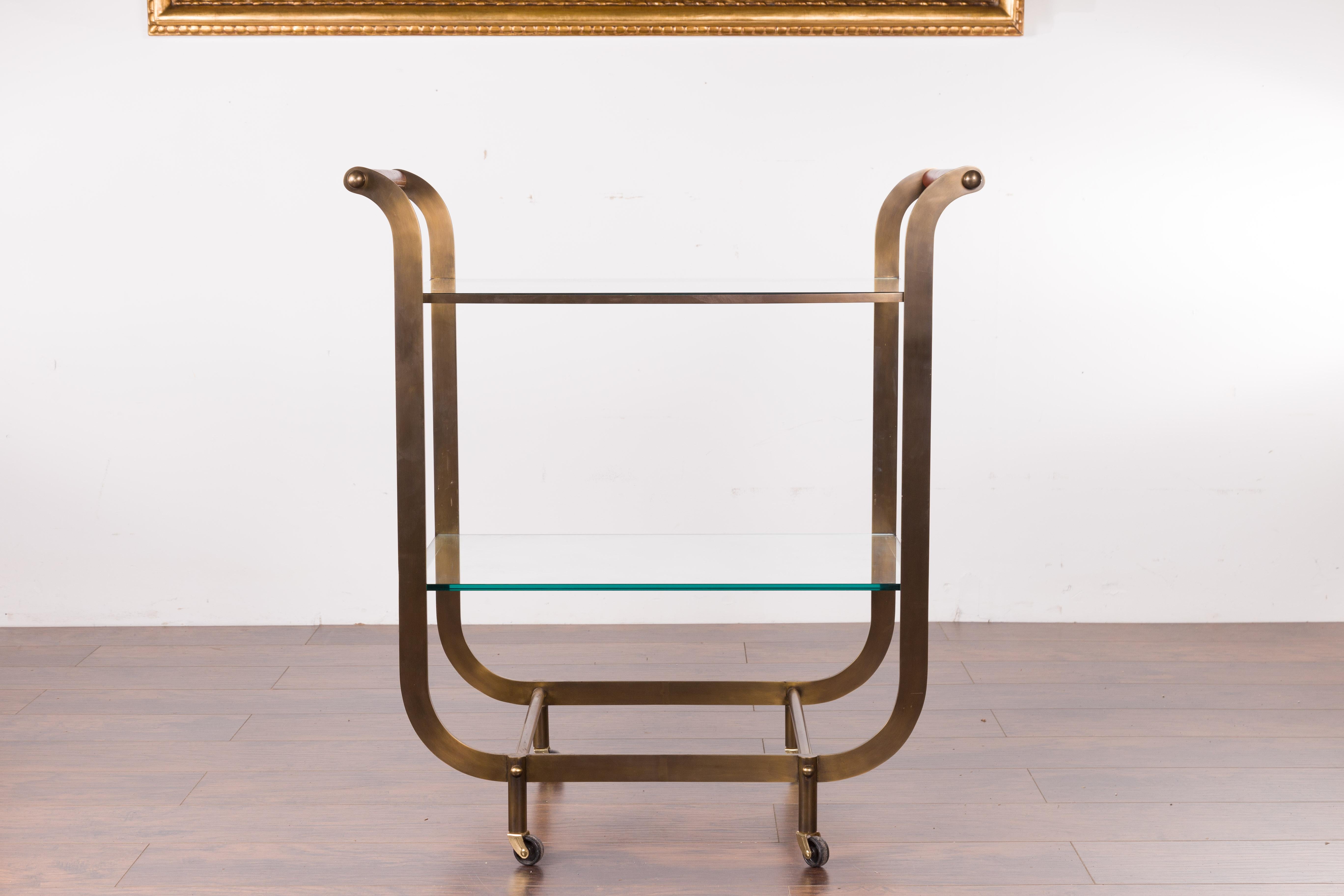 A French vintage brass tea cart from the mid-20th century with red leather handles and casters. Created in France during the mid-century period, this tea cart features delicately out-scrolling side supports accented with red leather handles.