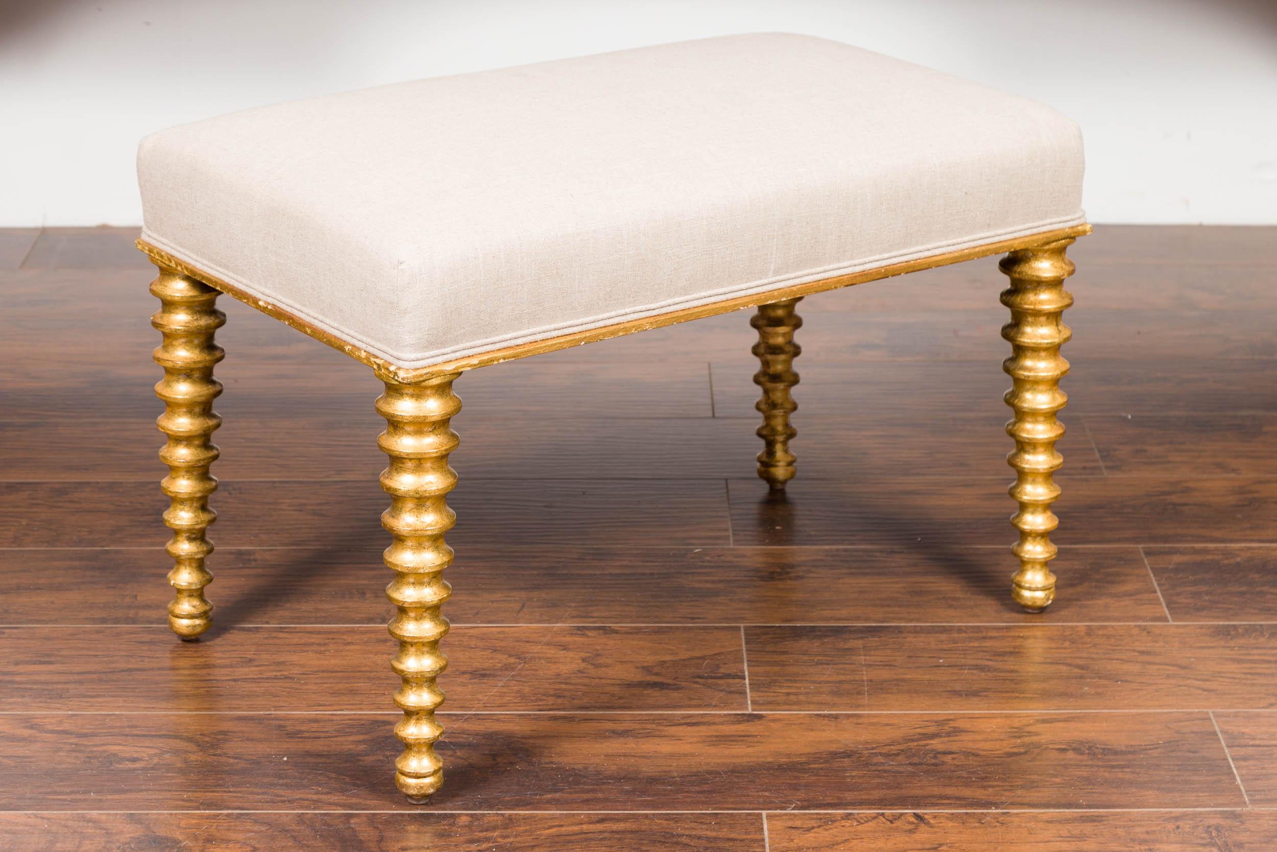A French giltwood stool from the mid-20th century, with spool legs and linen upholstery. Born in France during the midcentury period, this gilded stool features a rectangular seat that has been reupholstered with a new linen double welt fabric. The