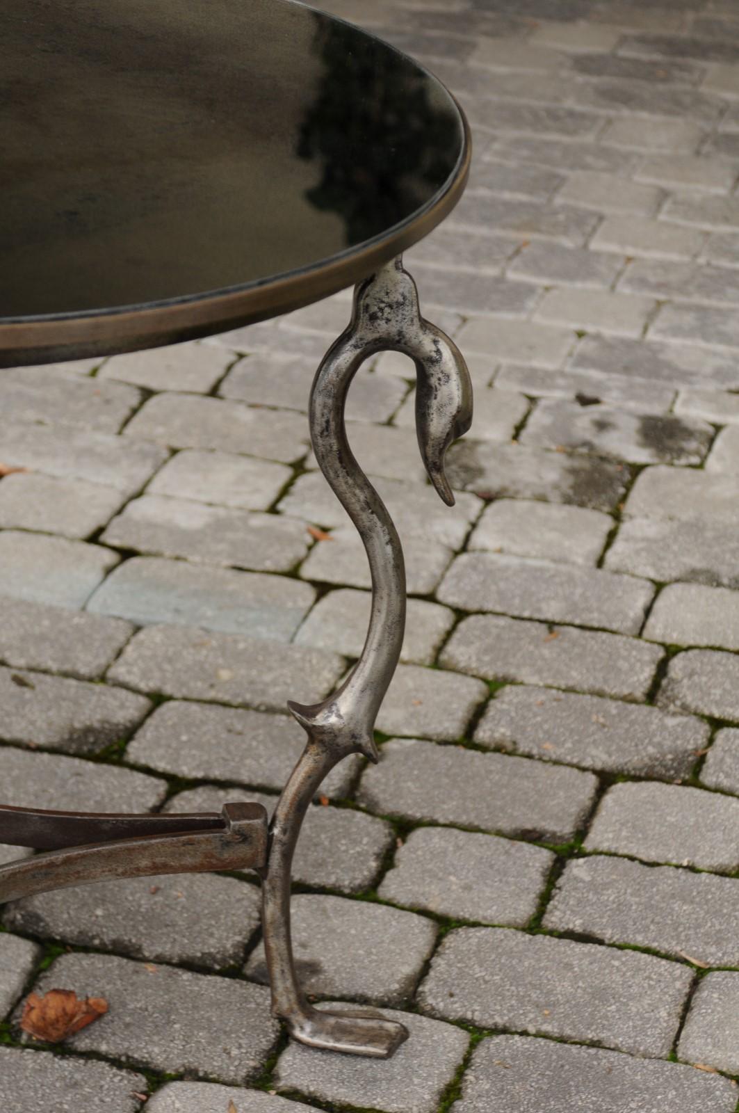 A French vintage steel round center table from the mid-20th century, with new mirrored top, swan motifs and duck feet. This French midcentury table features a circular top presenting a nicely antiqued mirror, delicately supported by three swan heads