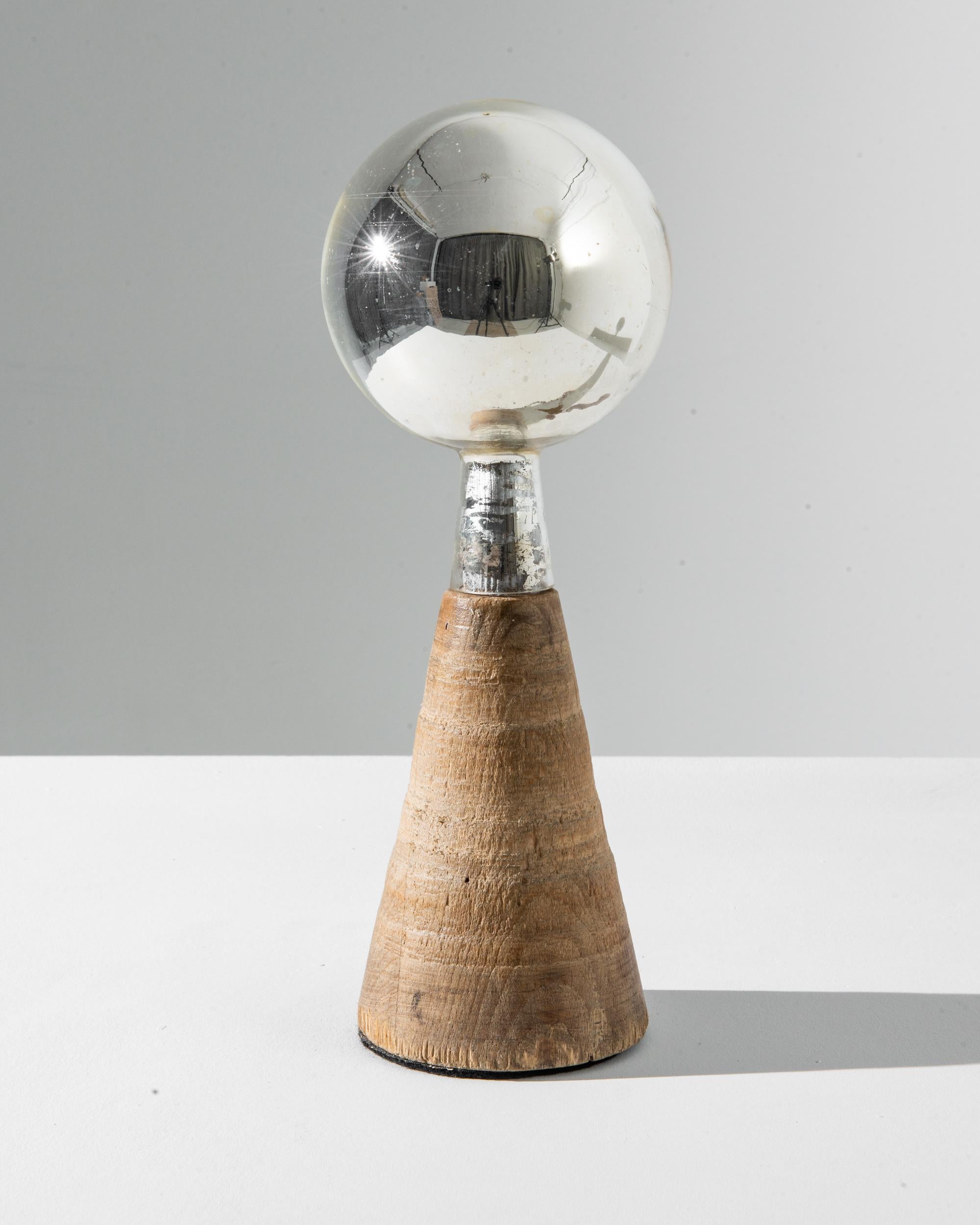Clear yet ethereal, this vintage wood and glass decoration makes an endlessly intriguing accent. Made in France in the 20th century, the composition has a graphic simplicity: a sphere of mercury glass sits atop a cone of natural wood. The silvered