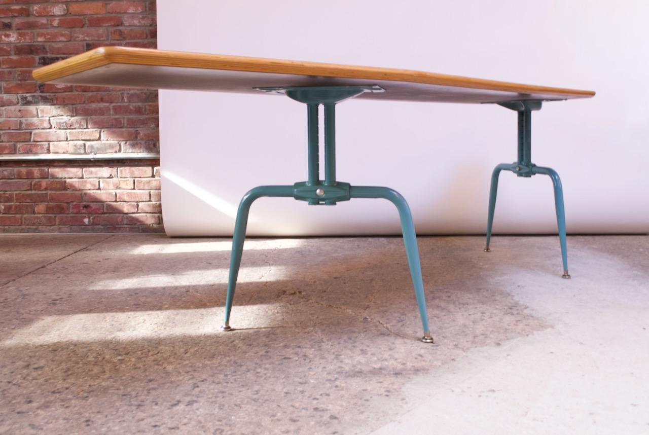 This unique 1950s French table is composed of a laminated plywood, asymmetrical top supported by enameled-steel bases which are adjustable. This versatile table can be used as a dining, conference, or writing table. The table bases are flared out in