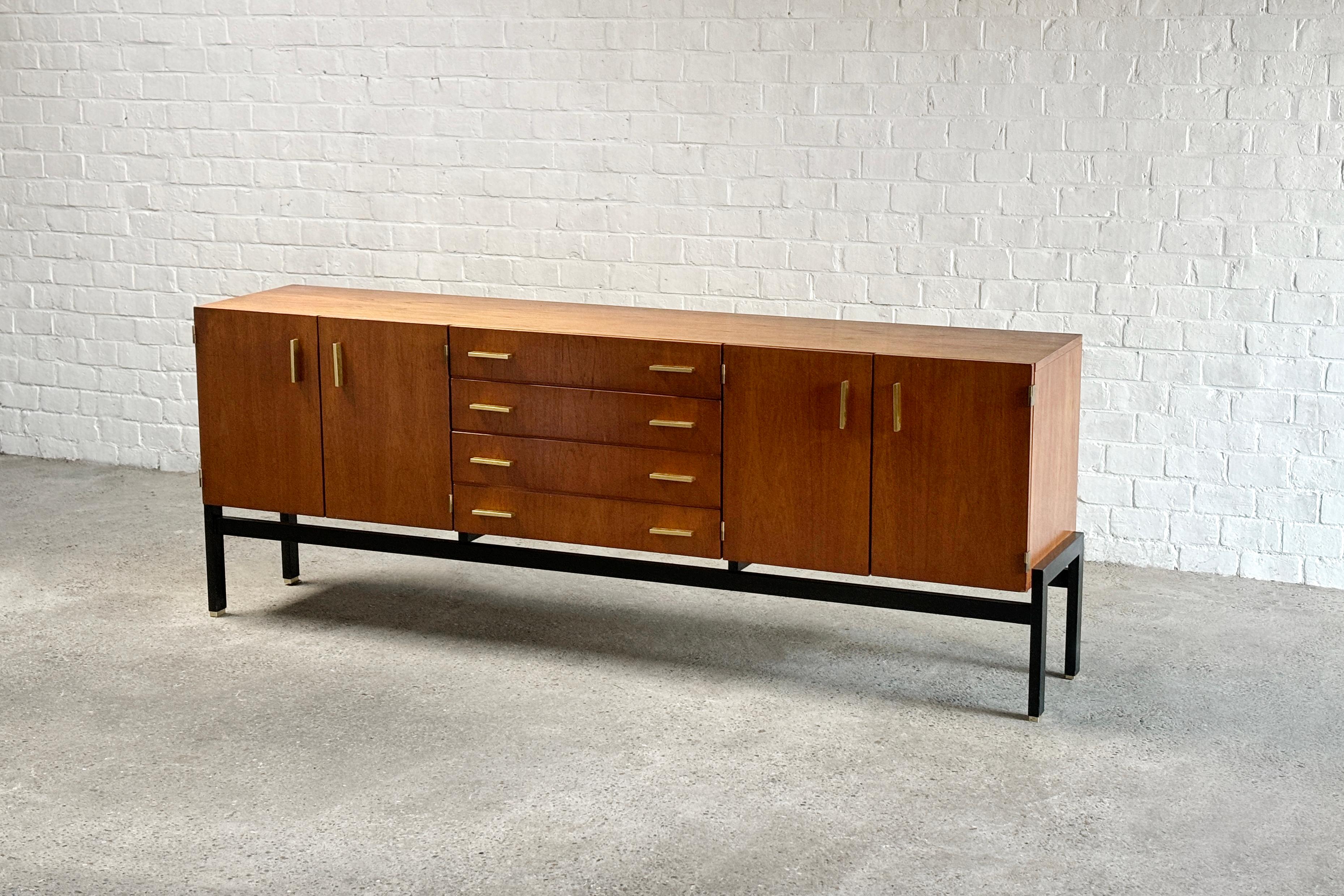 A stunning modernist french sideboard from the 1960s whose designer remains unknown. The sideboard has a teak veneer surface and features four doors and four drawers with rectangular brass handles, creating a modern look. The body rests on black