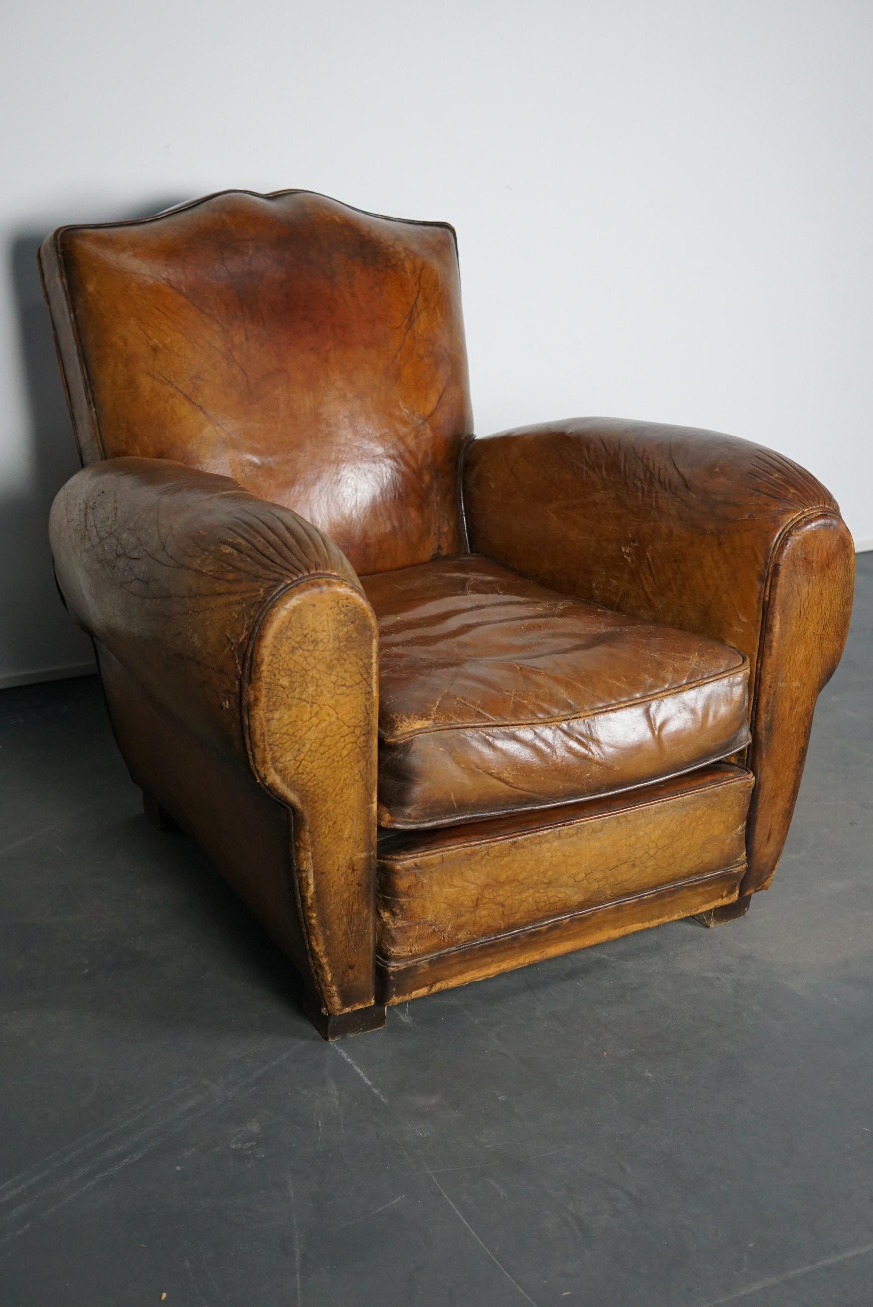 This cognac-colored leather club chair comes from France. It is upholstered with cognac-colored leather and features metal rivets and wooden legs.