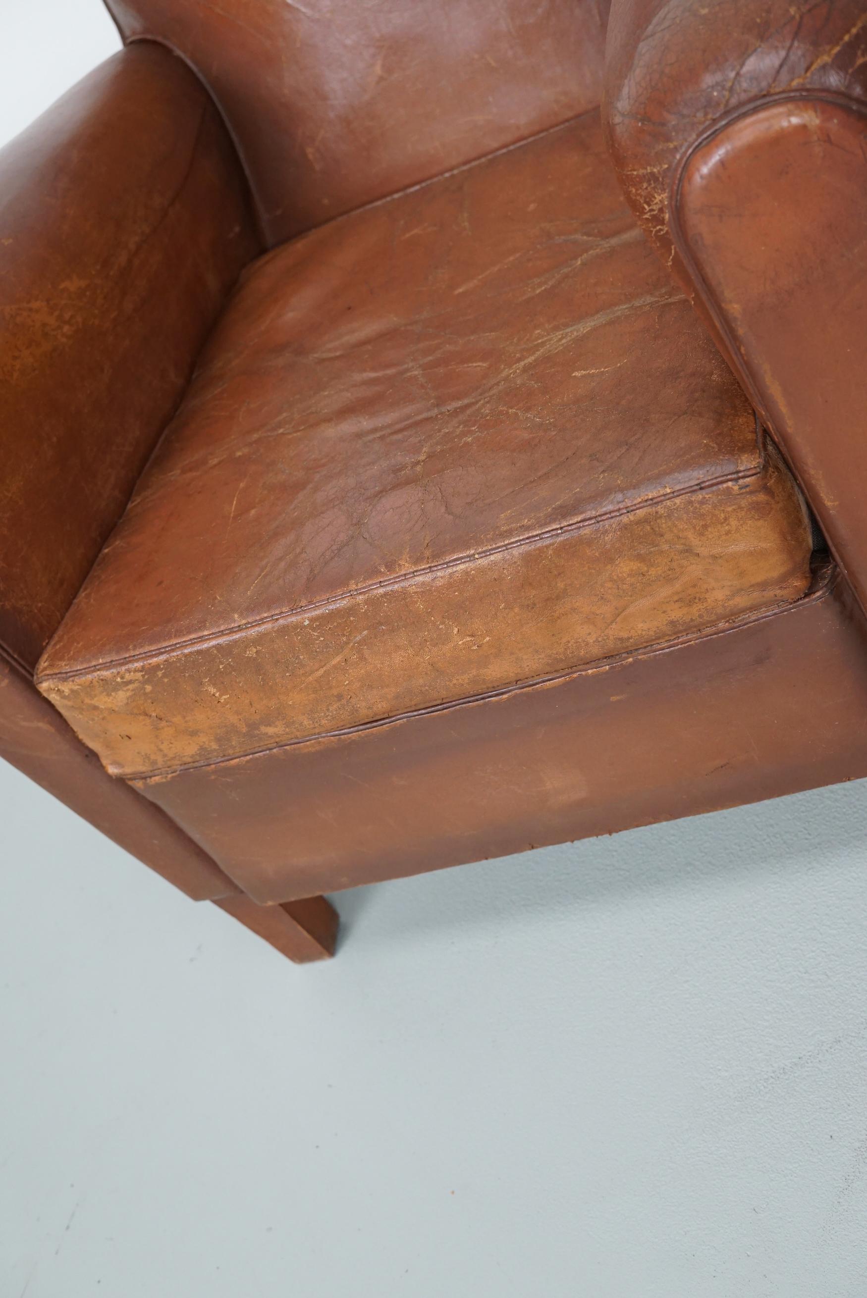 Ce fauteuil club en cuir de couleur cognac provient de France. Il est recouvert de cuir de couleur cognac et comporte des rivets en métal et des pieds en bois.