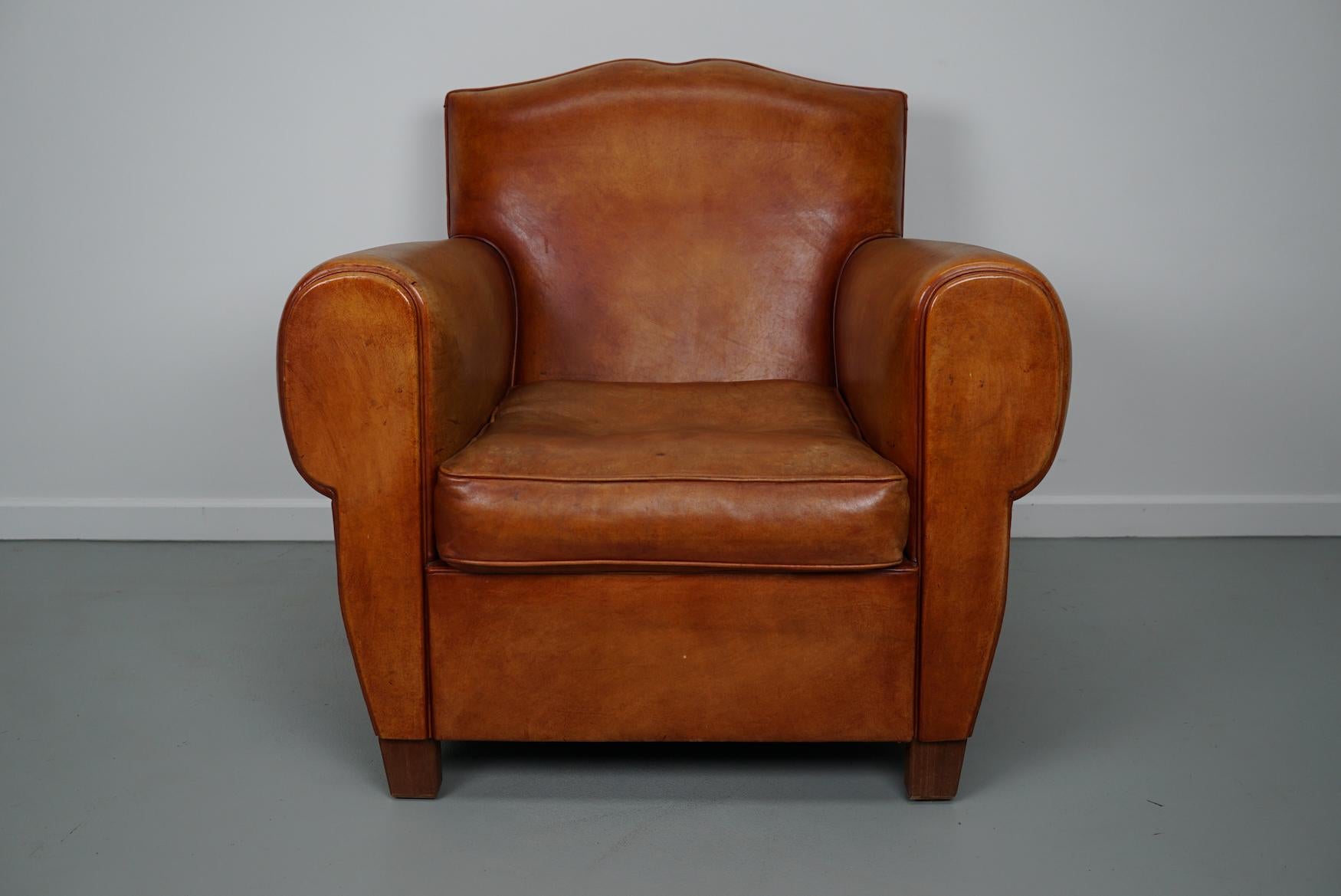 This cognac-colored leather club chair comes from France. It is upholstered with cognac-colored leather and features metal rivets and wooden legs.