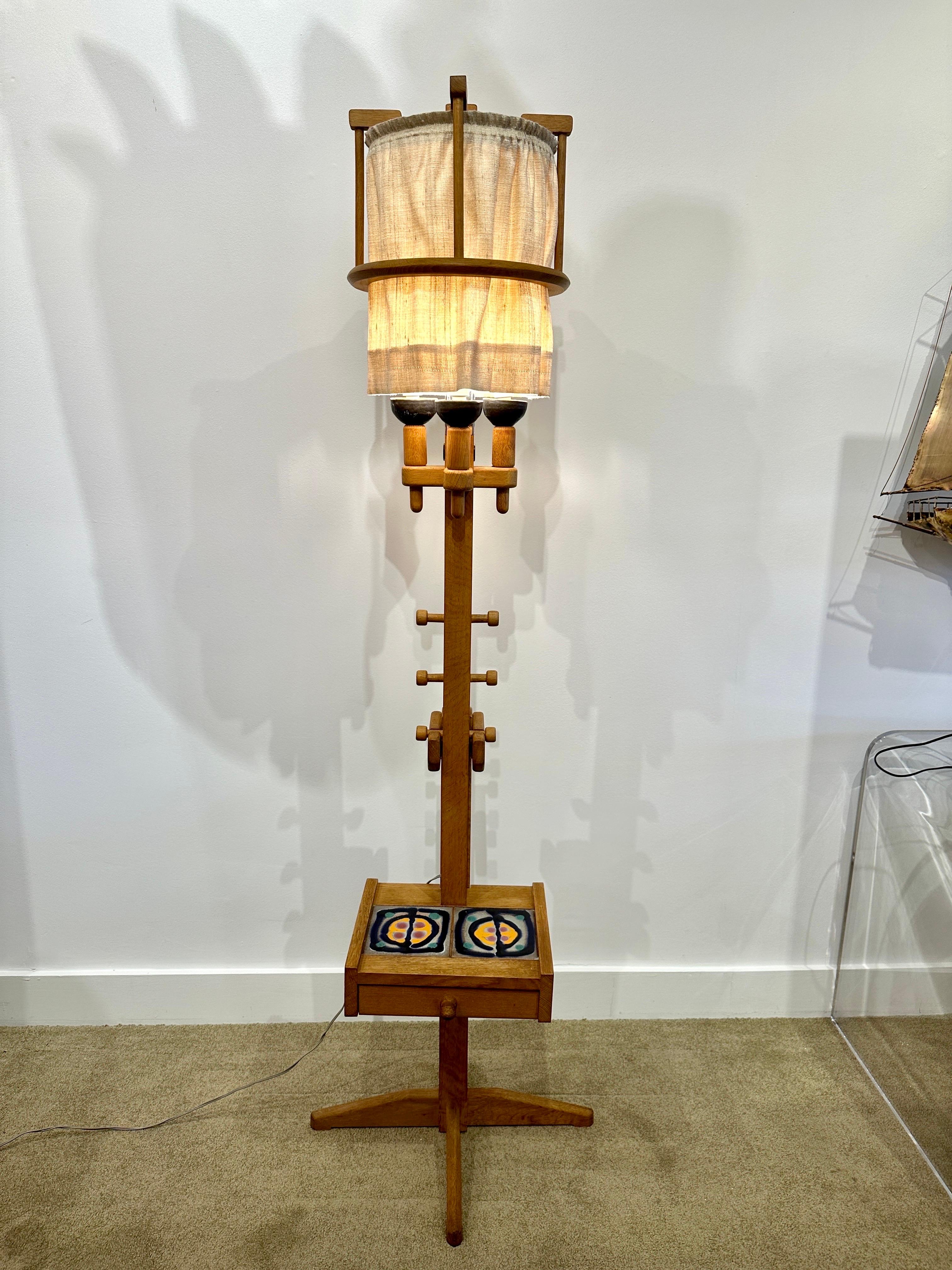 This very rare Guillerme et Chambron floor lamp in oak and hand made ceramic tile details has SO MANY unique details. The lamp itself is adjustable by height on 3 levels as seen in the video. The single drawer to base can be a side table between a
