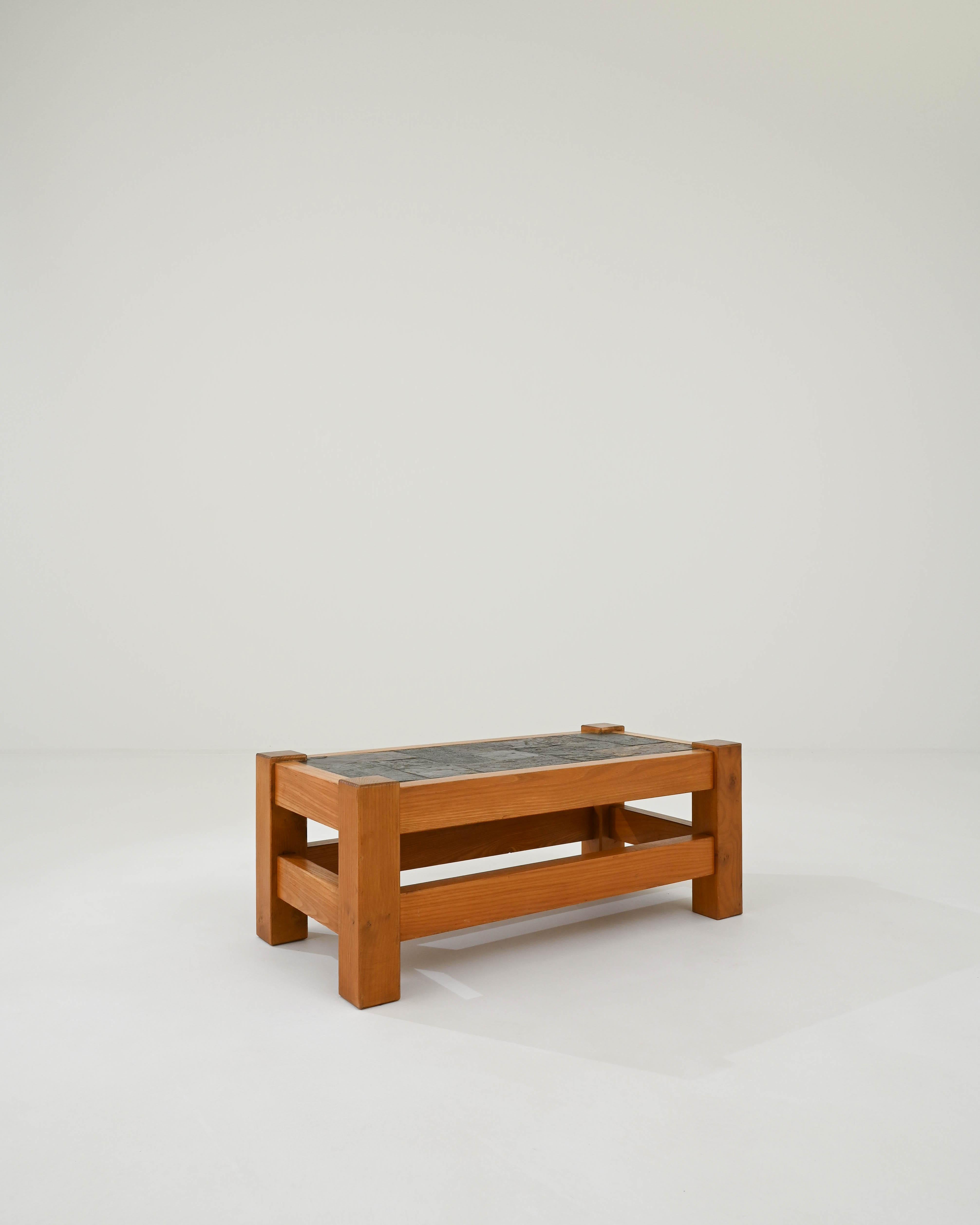 An oak coffee table with a tiled stone top produced in 20th Century France. This low table is designed in a rustic vein of the mid-century modern with a simple oak silhouette, combined with a black stone top for an image of elemental simplicity. The