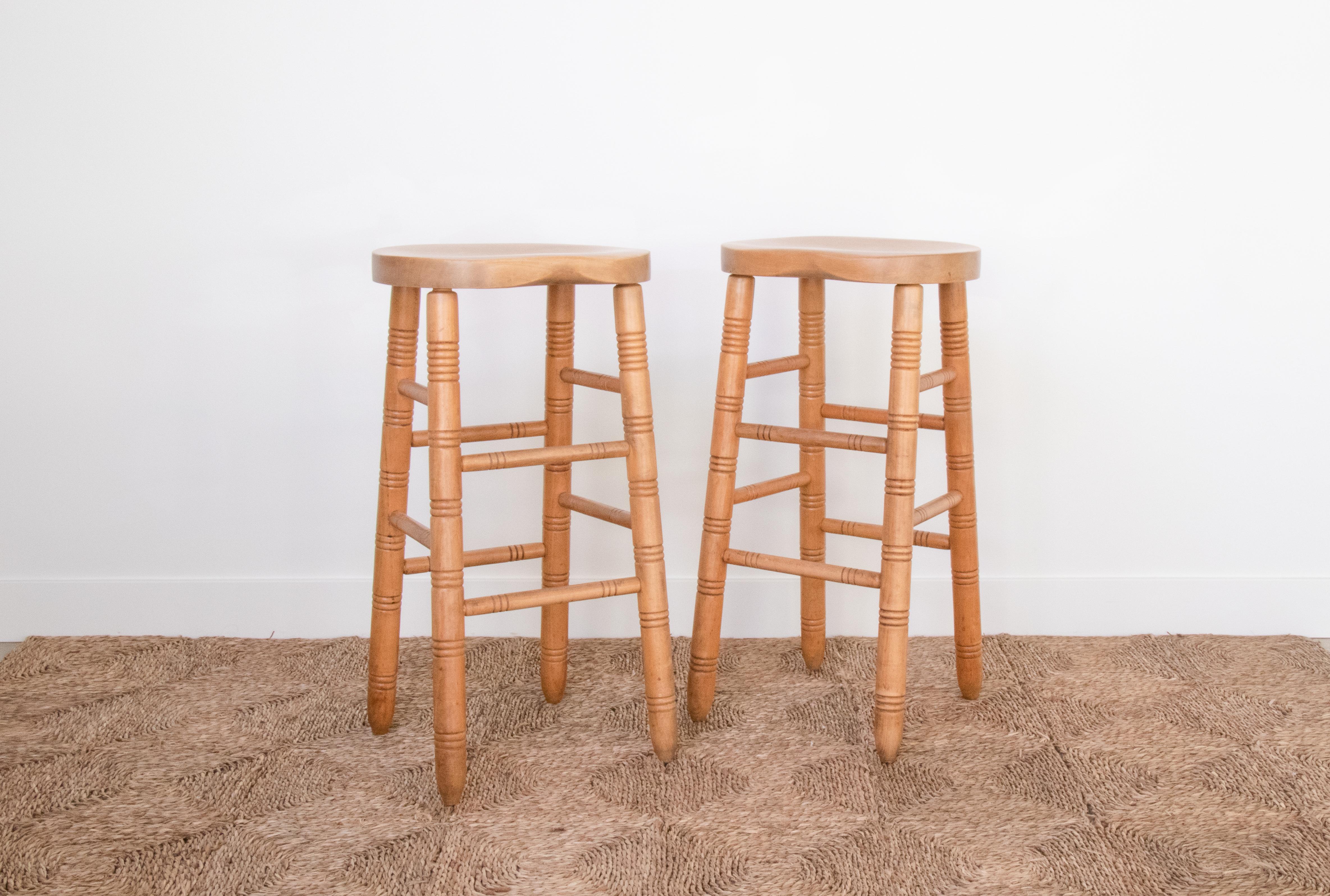 Set of two vintage French oak bar stools in the style of Charles Dudouyt from the 1940s. Carved wood seat and four post legs with carved ring details. Slim support bars and footrest with same carved detail. Beautiful and unique detail with original