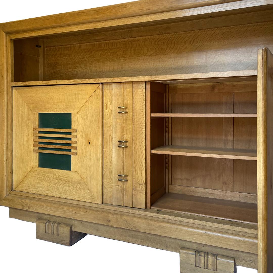 A substantially sized oak cabinet with distinctive details and brass hardware, attributed to the French designer and architect Charles Dudouyt. Thoughtfully designed in the 1940s, the left and right green leather fronted panel doors open to reveal 3