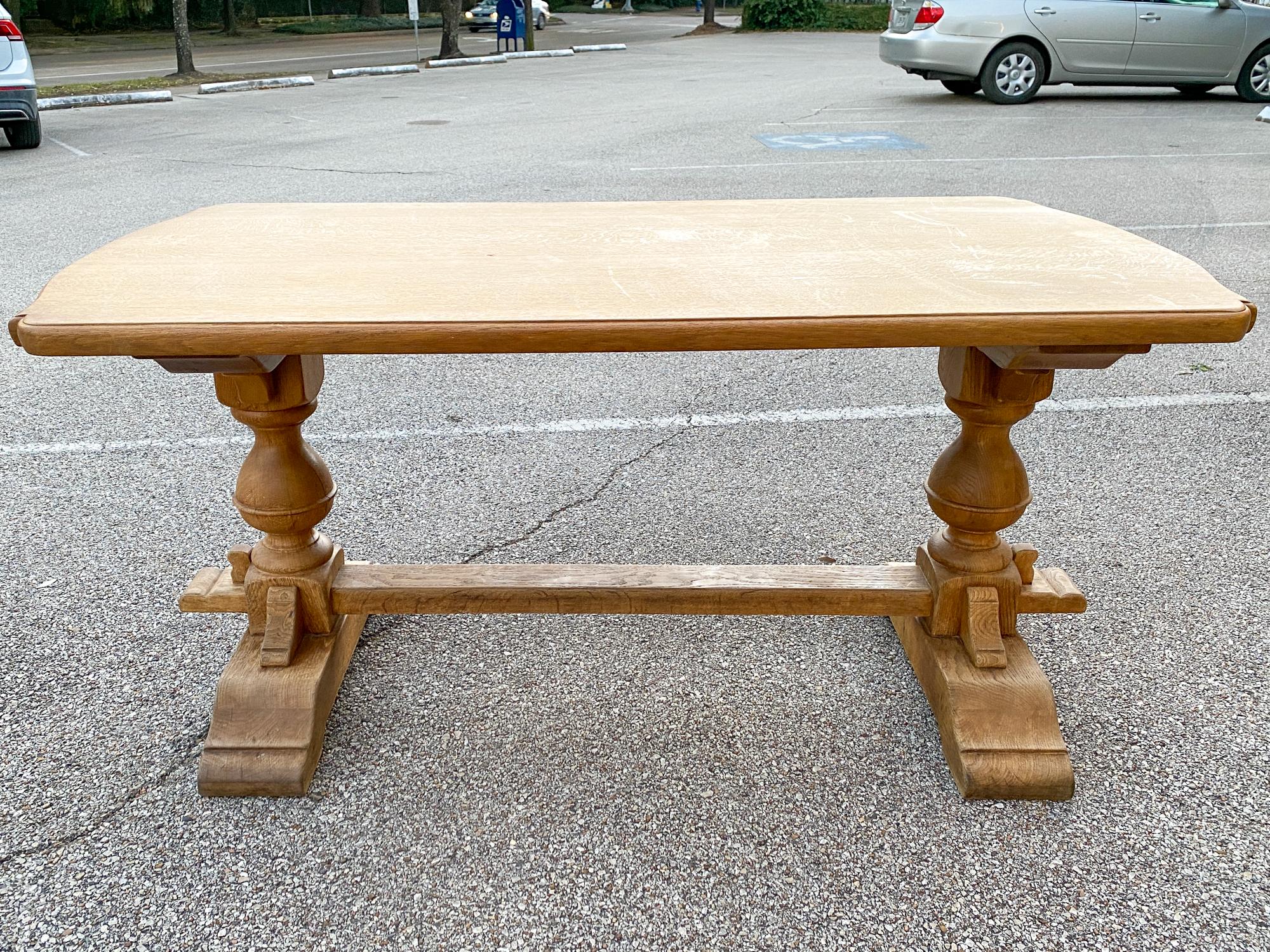 This vintage French Oak table features a double-pedestal leg design with a stretcher and chunky turned details. The top has a decorative edge and is an ideal size for use as a desk. The top can be secured to the base via the steel rails that have