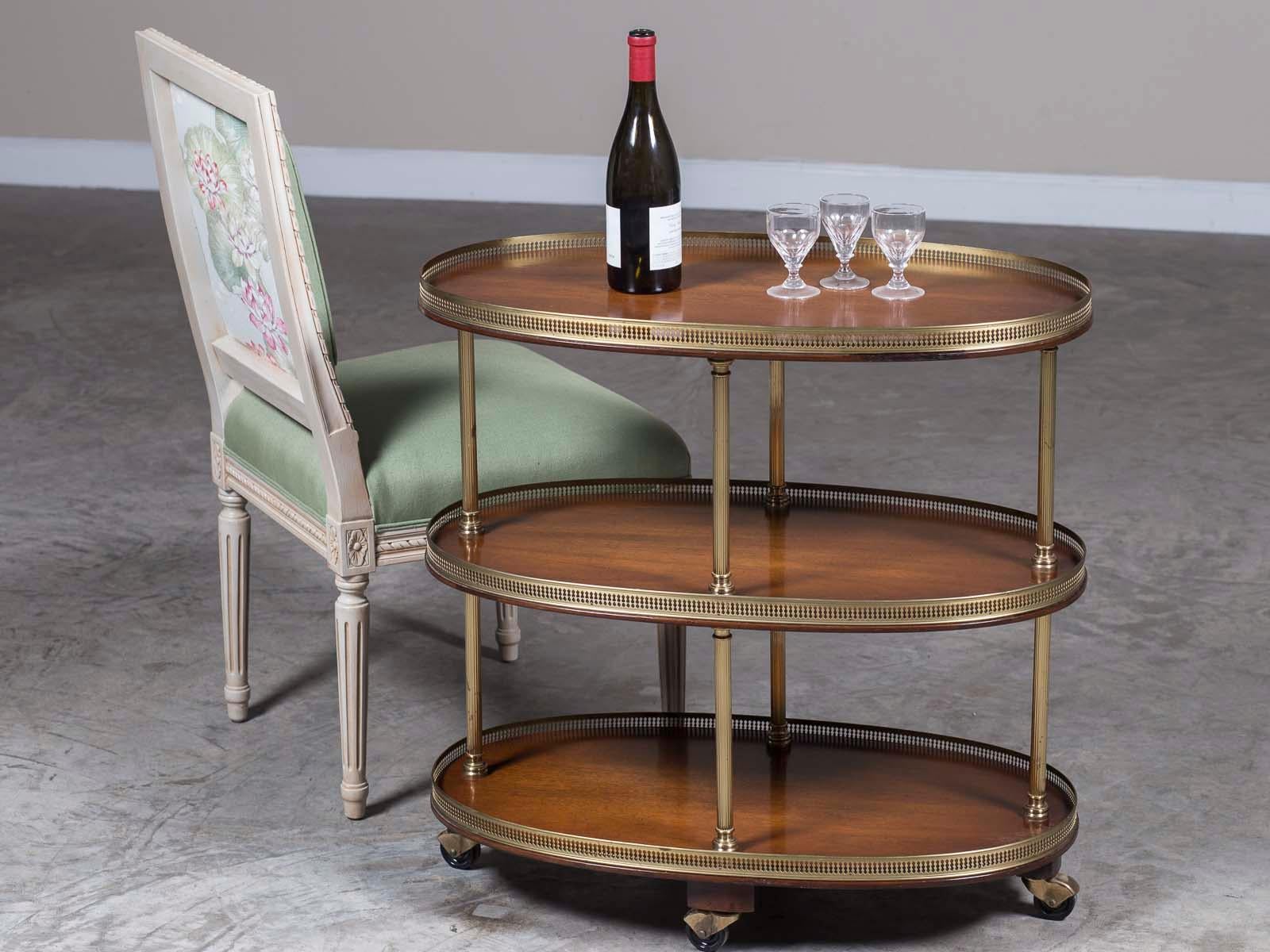 A vintage French oval mahogany and brass three tier rolling cart circa 1970 with a gallery rail on all three levels. This attractive and simple bar cart is set on four casters as it was designed to be moved about an interior as needed. Please use