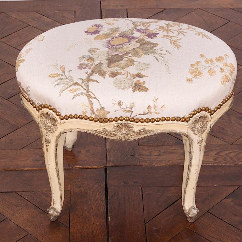 A vintage French Louis XV style finely carved stool with a painted and gilt finish and recent upholstery. Elegant cabriole legs and scrolled feet and fine carved shell motif details.