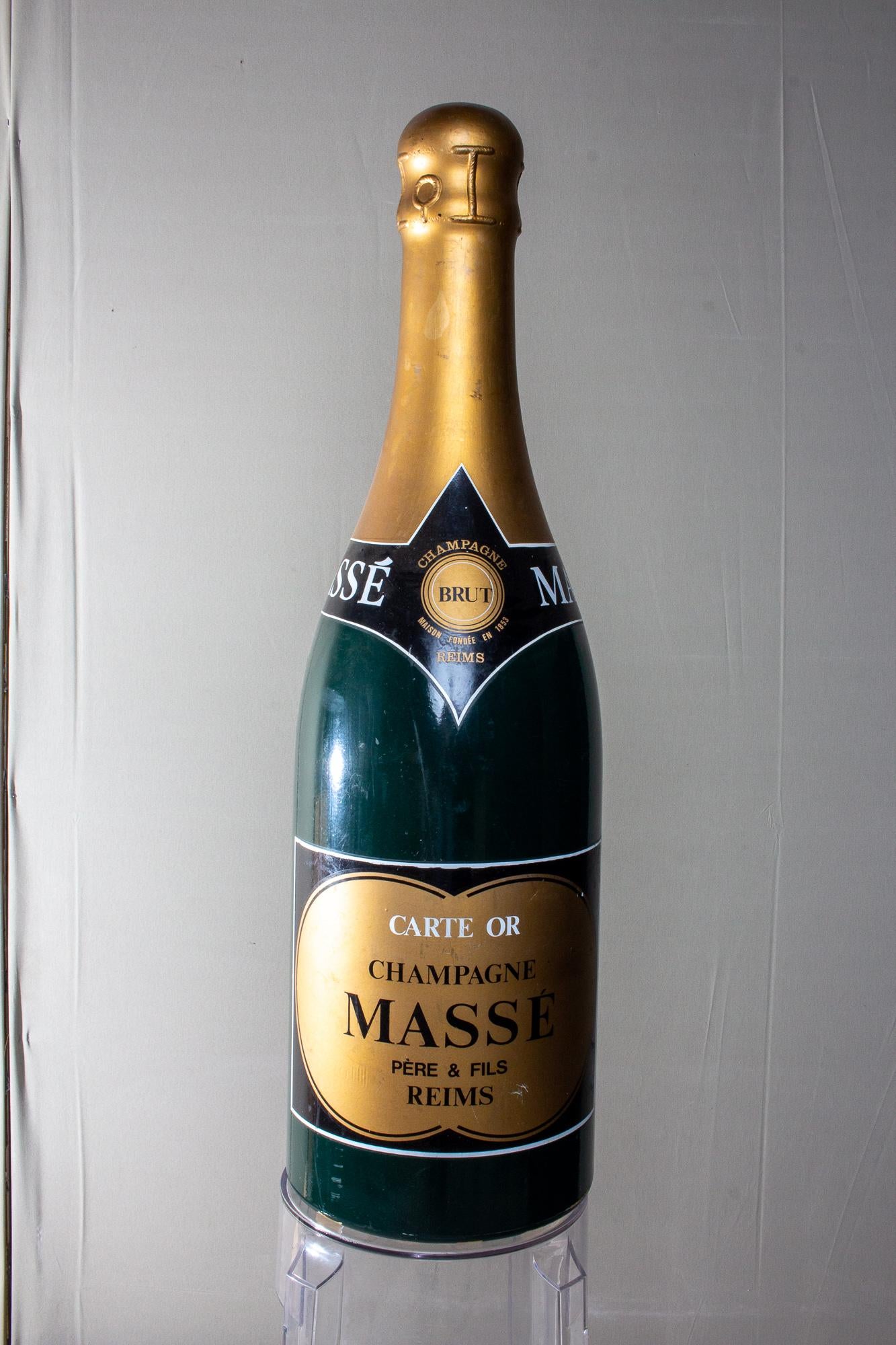 A large, vintage champagne bottle prop from Champagne Massé Pére & Fils in Reims, France. This piece looks great for decoration on your bar top, or to prep your home for a New Year's Eve party. Large, deep green bottle with a gold label. Lightweight