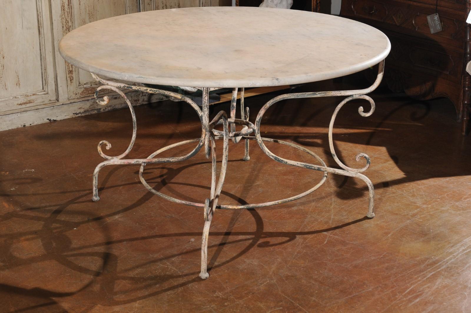 A vintage French painted iron garden table from the mid-20th century, with marble top and scrolling base. Born in France during the midcentury period, this charming garden table features a circular veined marble top sitting above a scrolling base