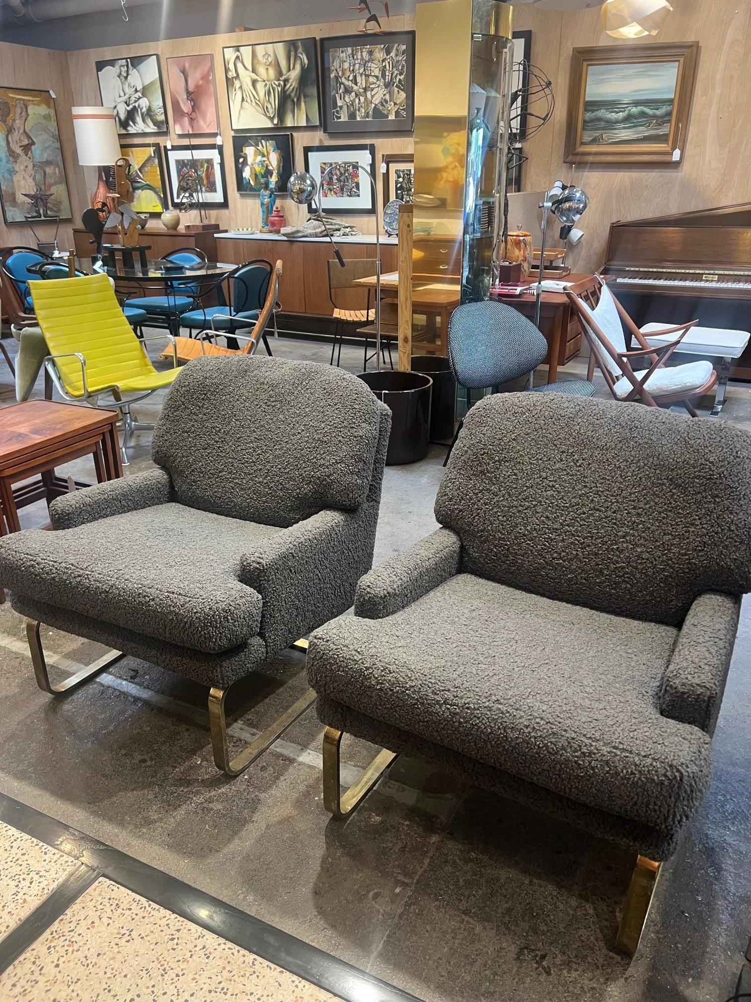A beautiful pair of Boucle Lounge chairs. They rest on a brass base and feature low armrests, ample seat cushions and offer incredible back support. Truly comfortable and effortlessly stylish! 