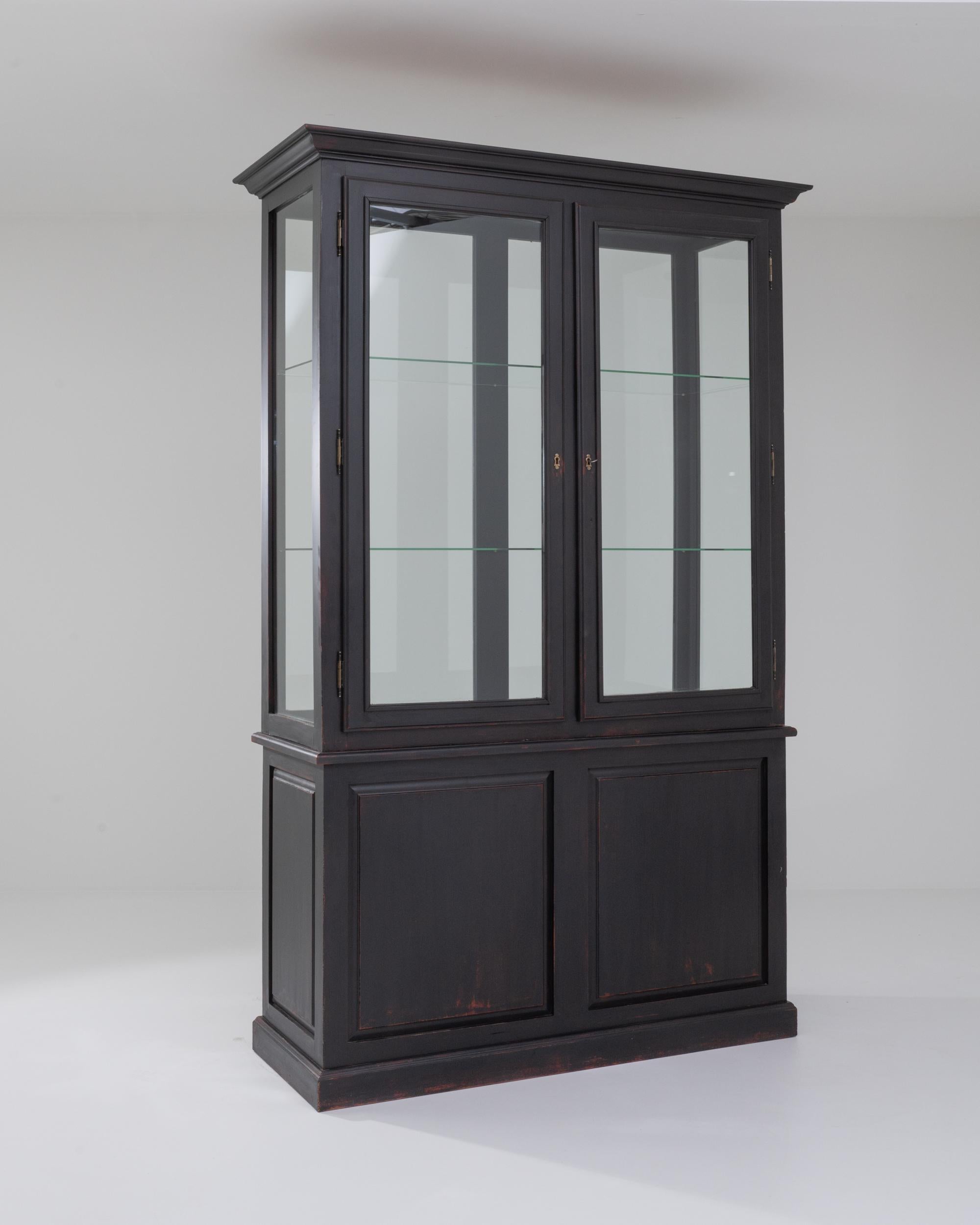 Tall and elegant, this vintage vitrine makes an ideal display case. Built in France in the 20th century, the design has an attractive simplicity: clean lines and the stylish black finish of the wood astutely frame the glass shelves without