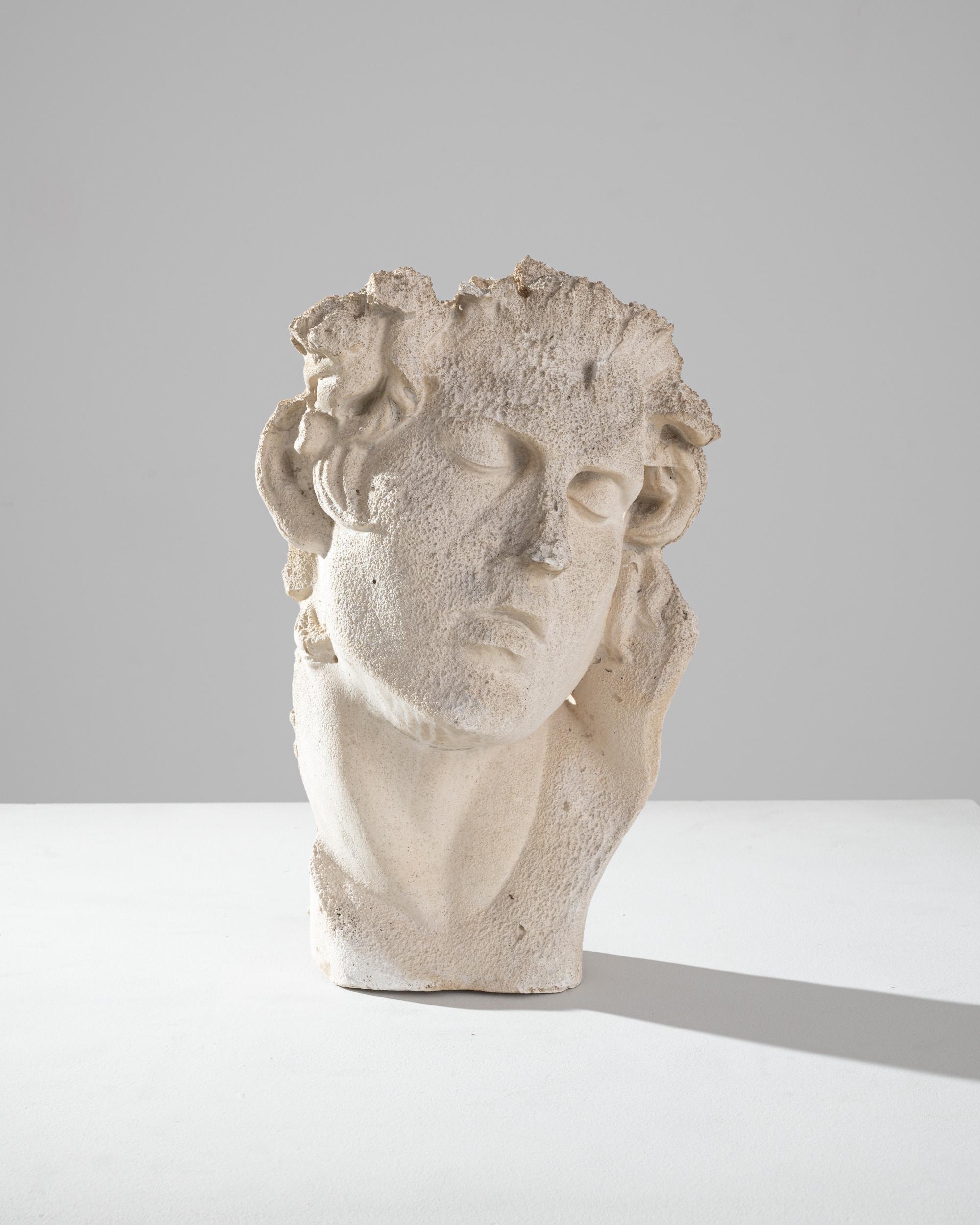 This vintage plaster sculpture depicts the head of a beautiful youth, staring into the distance with a melancholy expression. Made in France in the 20th century, the style emulates that of ancient Greek and Roman statues. The features of the face