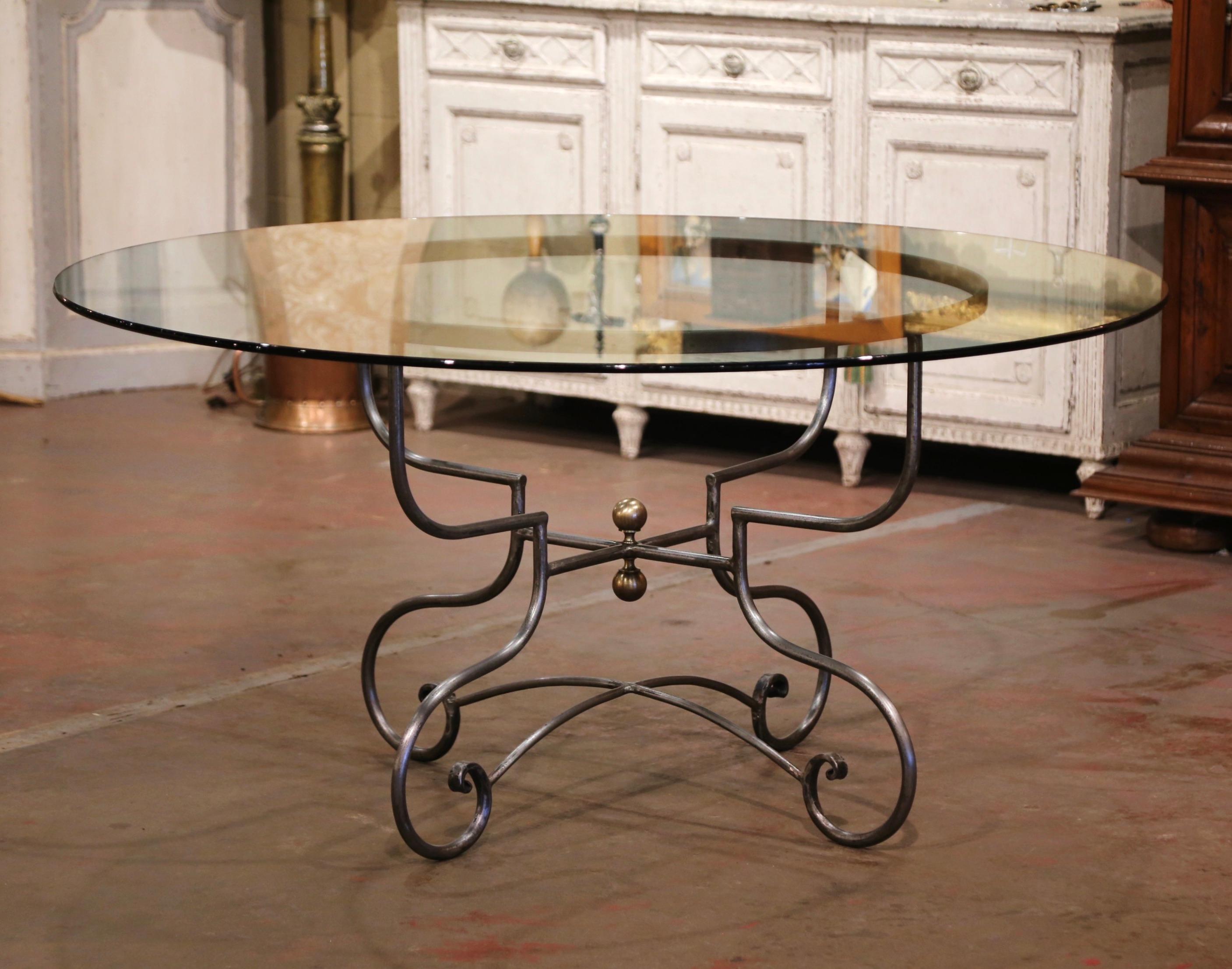 Decorate a dining or breakfast room with this elegant table. Crafted in Paris France circa 1980, the table features a wrought iron base with scrolled legs decorated with a double bottom stretcher embellished with a center brass finial. The surface