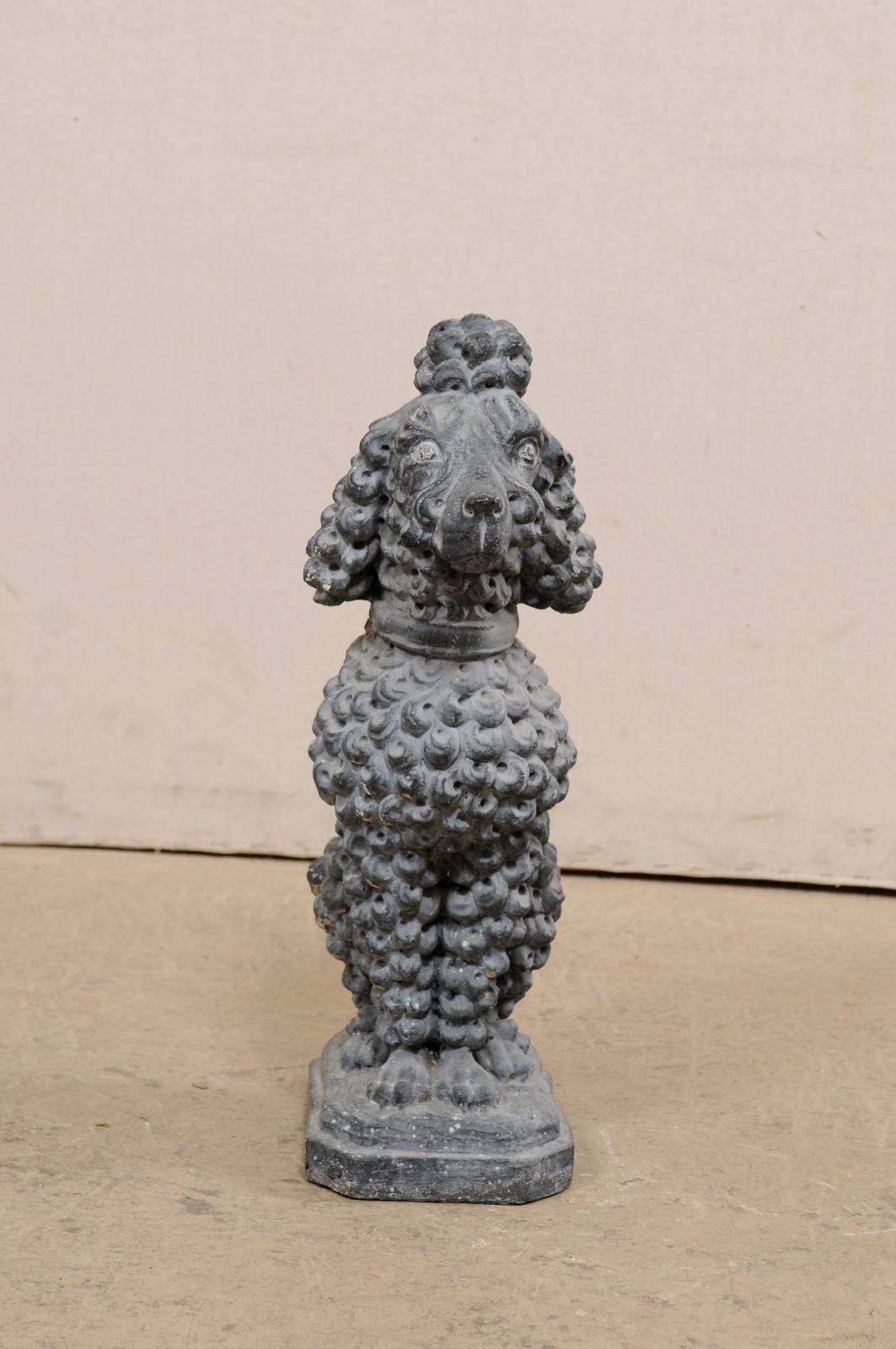 A French vintage cast stone poodle statue. This sweet little dog statue from France, created of cast stone, depicts a poodle in seated position, looking straight ahead, face expressive and alert, with it's nicely quaffed haircut and pom-pom adorning