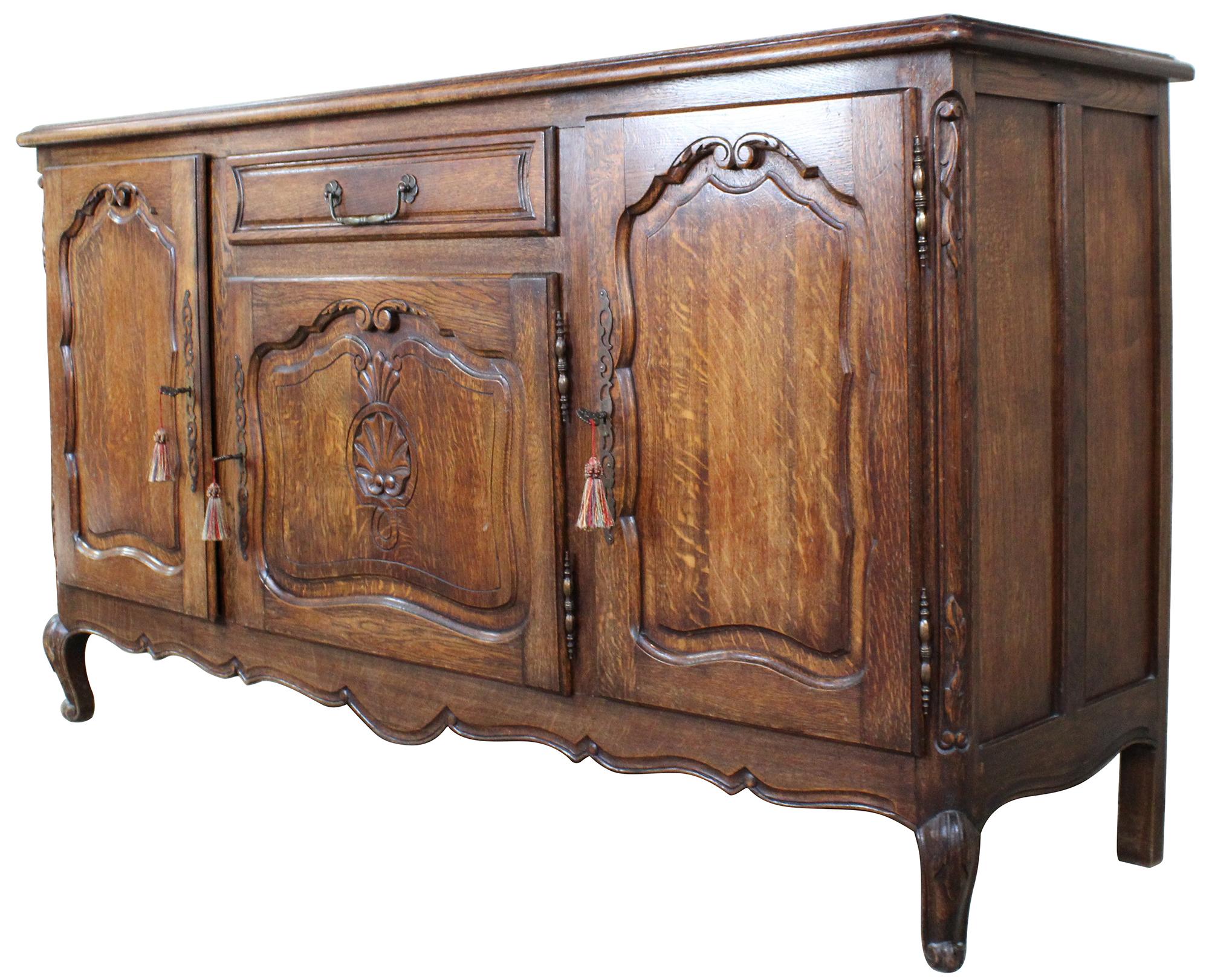 Belgian made oak sideboard, circa 1970s. Features French provincial styling with quartersawn (tiger) oak paneling. Includes 3 lockable cabinets, central drawer for flatware. Scalloped and scrolled accents. The cabinet is supported by cabriole legs