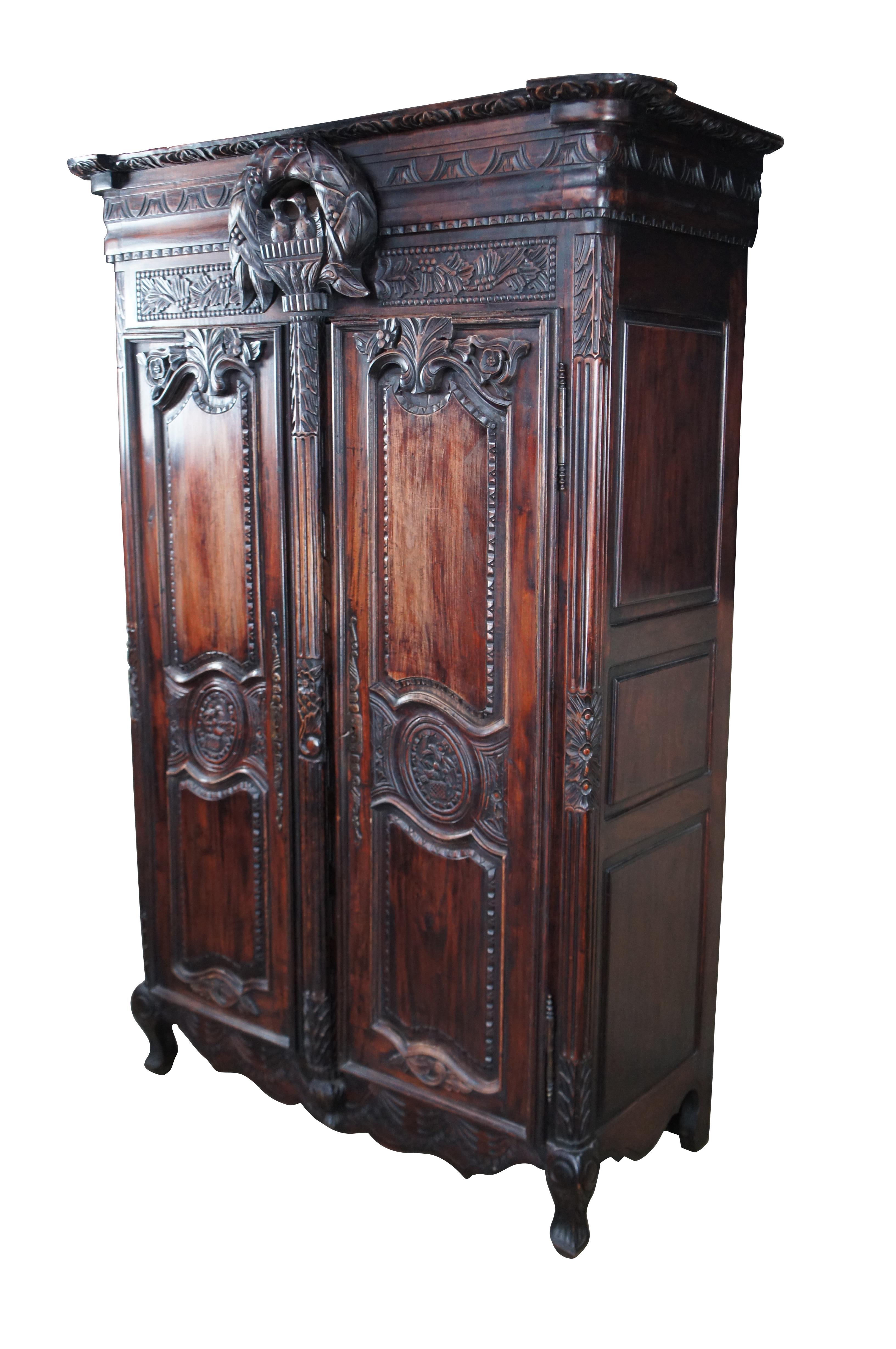 Vintage French Louis XV / Provincial style wedding armoire / wardrobe / linen press, circa last quarter 20th century.  Made of mahogany featuring baroque styling with carved egg and dart crown over a floral bird theme wreath and paneled doors with