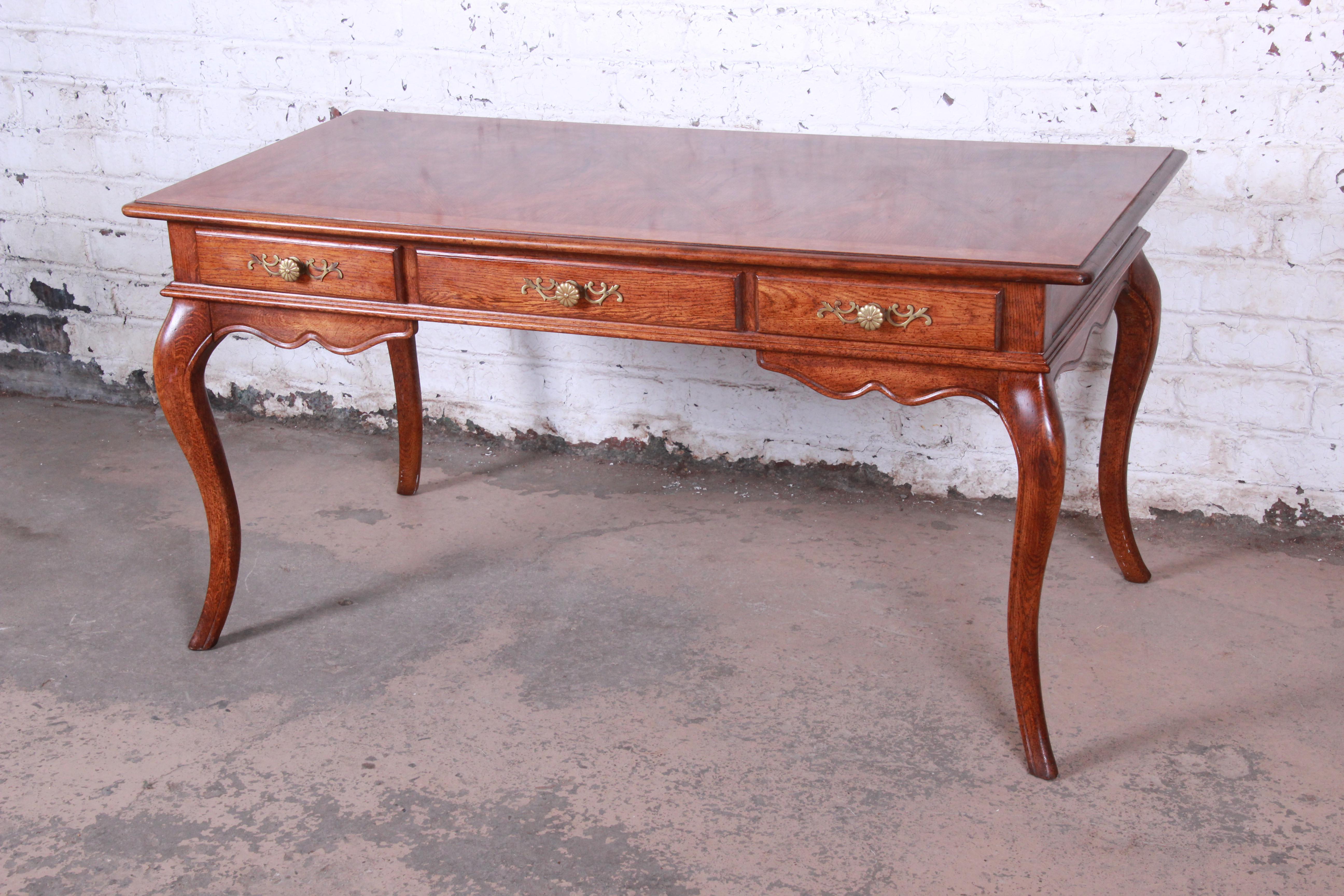 A beautiful vintage French Provincial Louis XV style writing desk by Hickory Manufacturing Co. The desk features nice oakwood grain with a gorgeous parquetry design on the top writing surface. It offers good storage, with three dovetailed drawers.