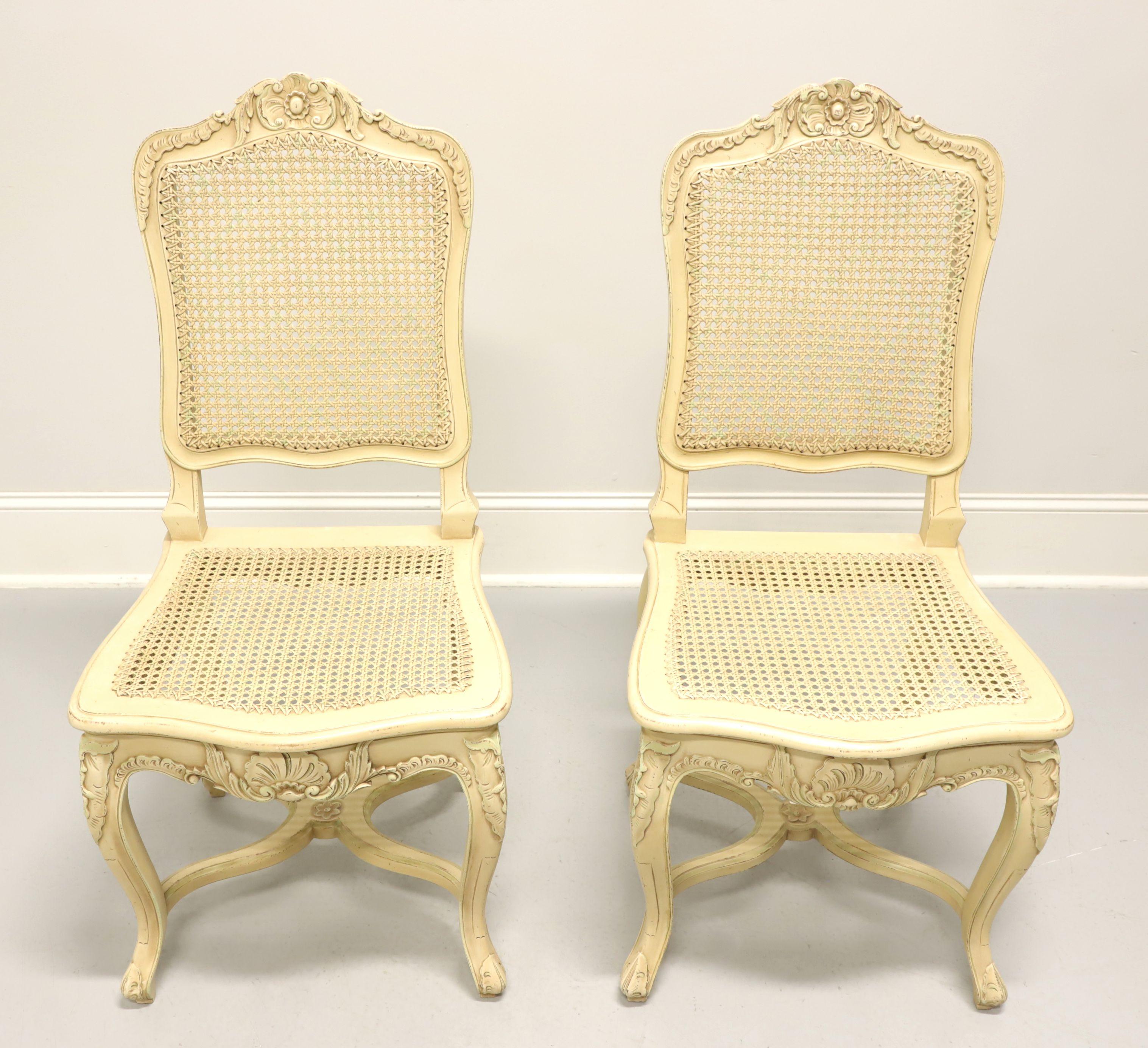 A pair of French Provincial style dining side chairs, unbranded, similar quality to Drexel. Solid wood painted an antique white with a slight distressing, decoratively carved crest rail, cane back & seat, carved apron & knees, curved legs and