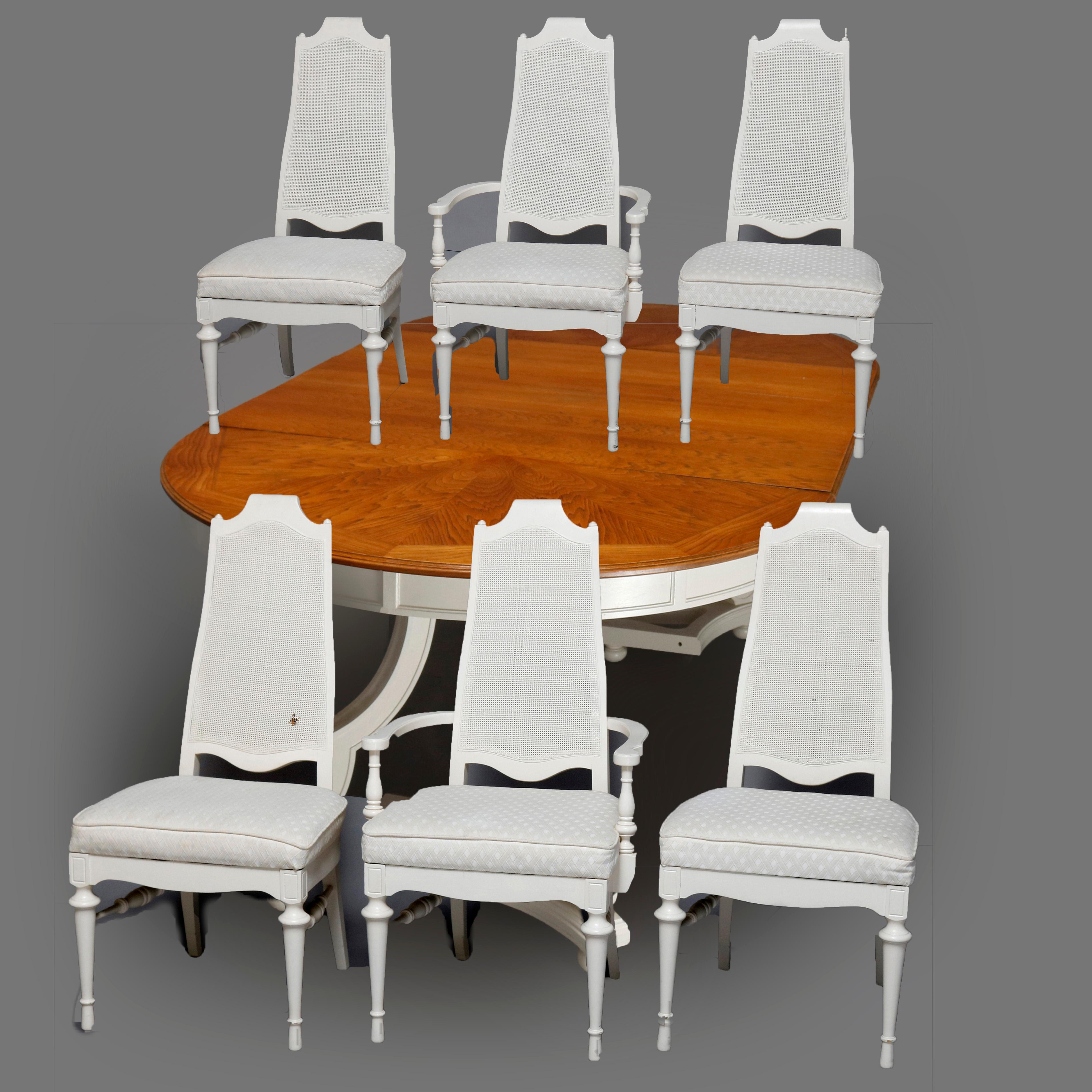 A vintage French Provincial style dining set offers white paint decorated chairs having tall pressed caned backs with scroll crest flanked by turned finials surmounting padded seats and raised on turned stylized urn form legs. Table with natural