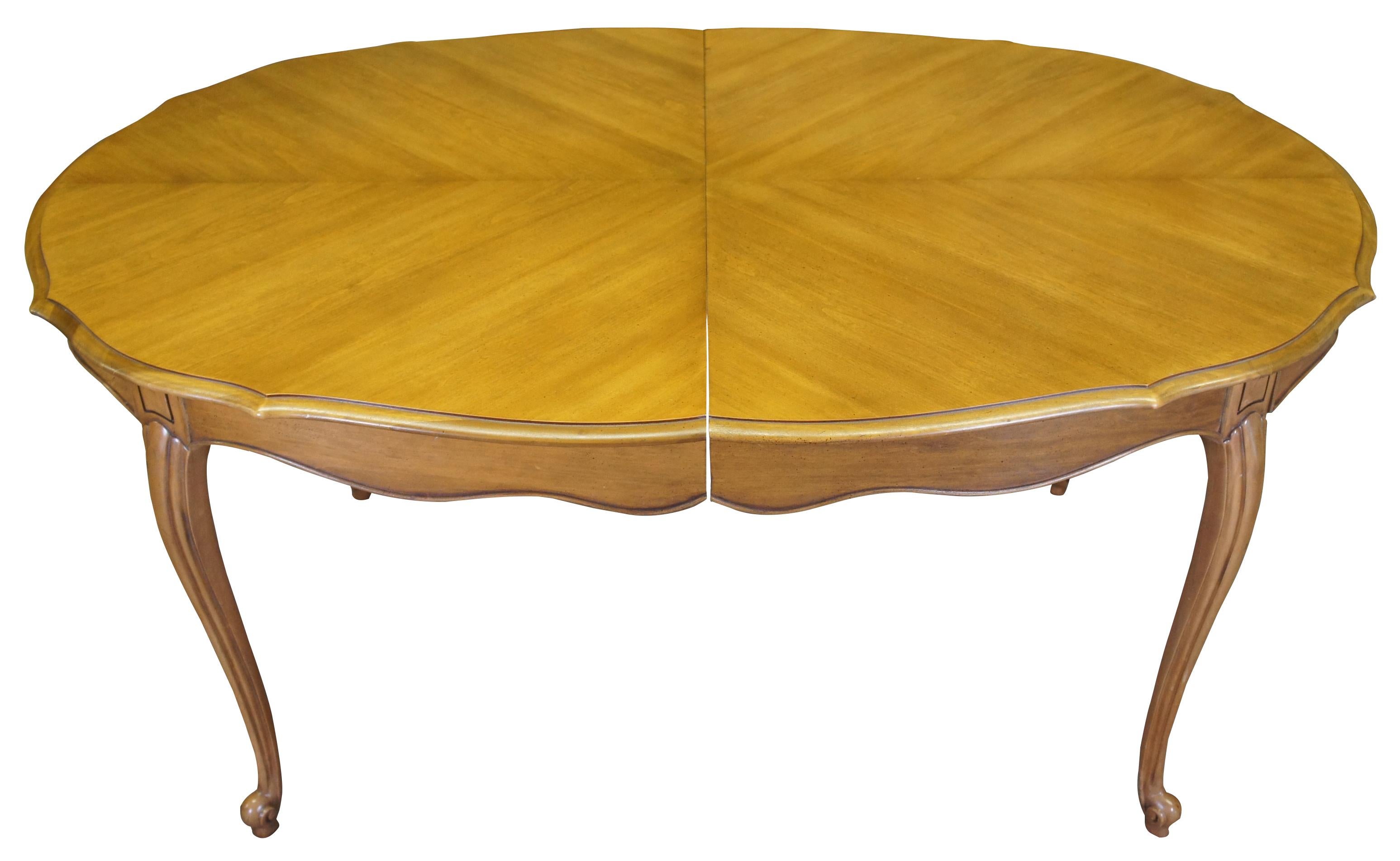 Mid 20th century French Provincial dining table. Made from walnut with an oval form featuring a scalloped top with matchbook veneer and long scrolled french legs. Extends to 101